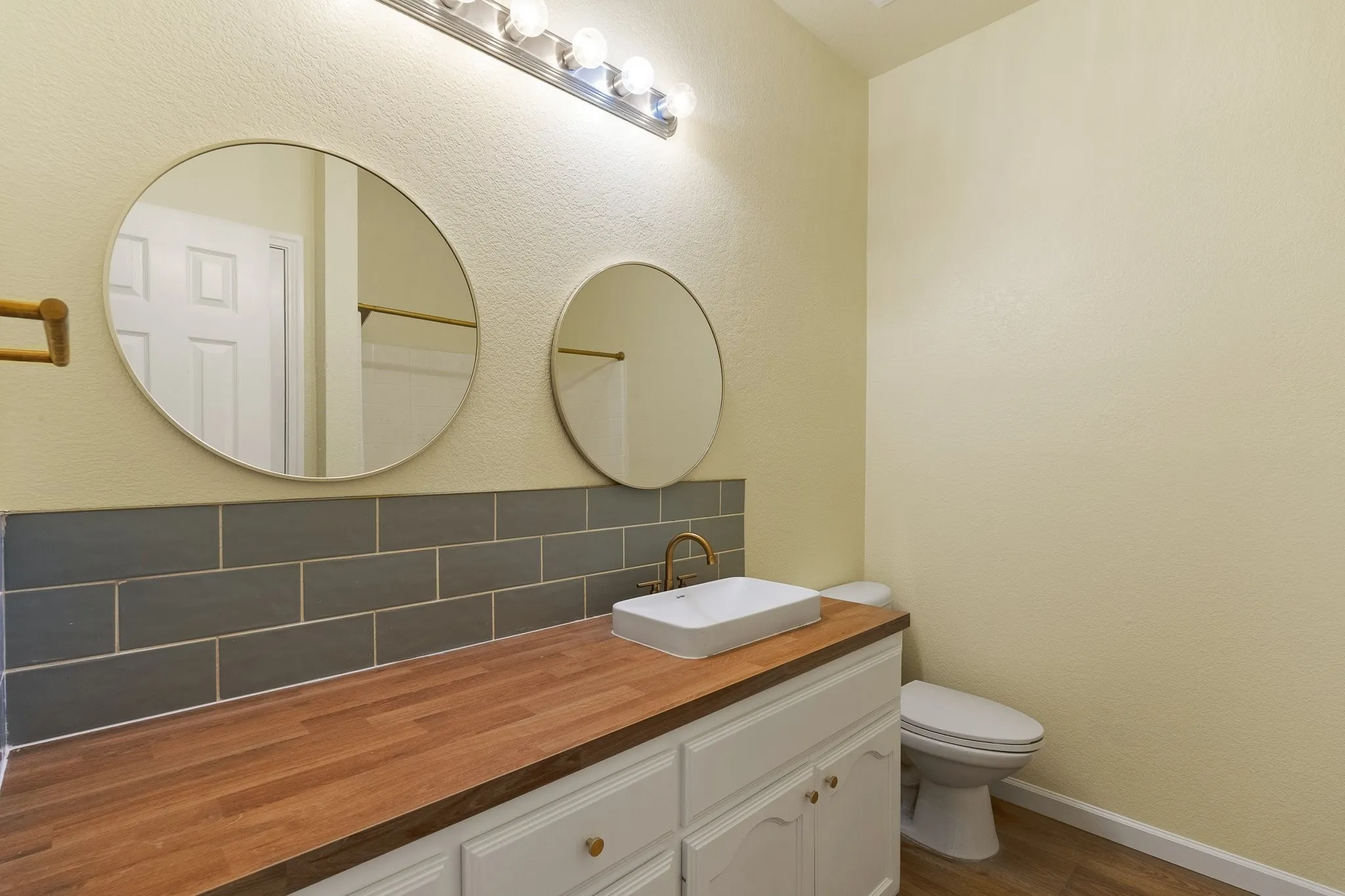 White shaker-style vanity with wood-finish countertop, rectangular vessel sink, and gold-tone fixtures
