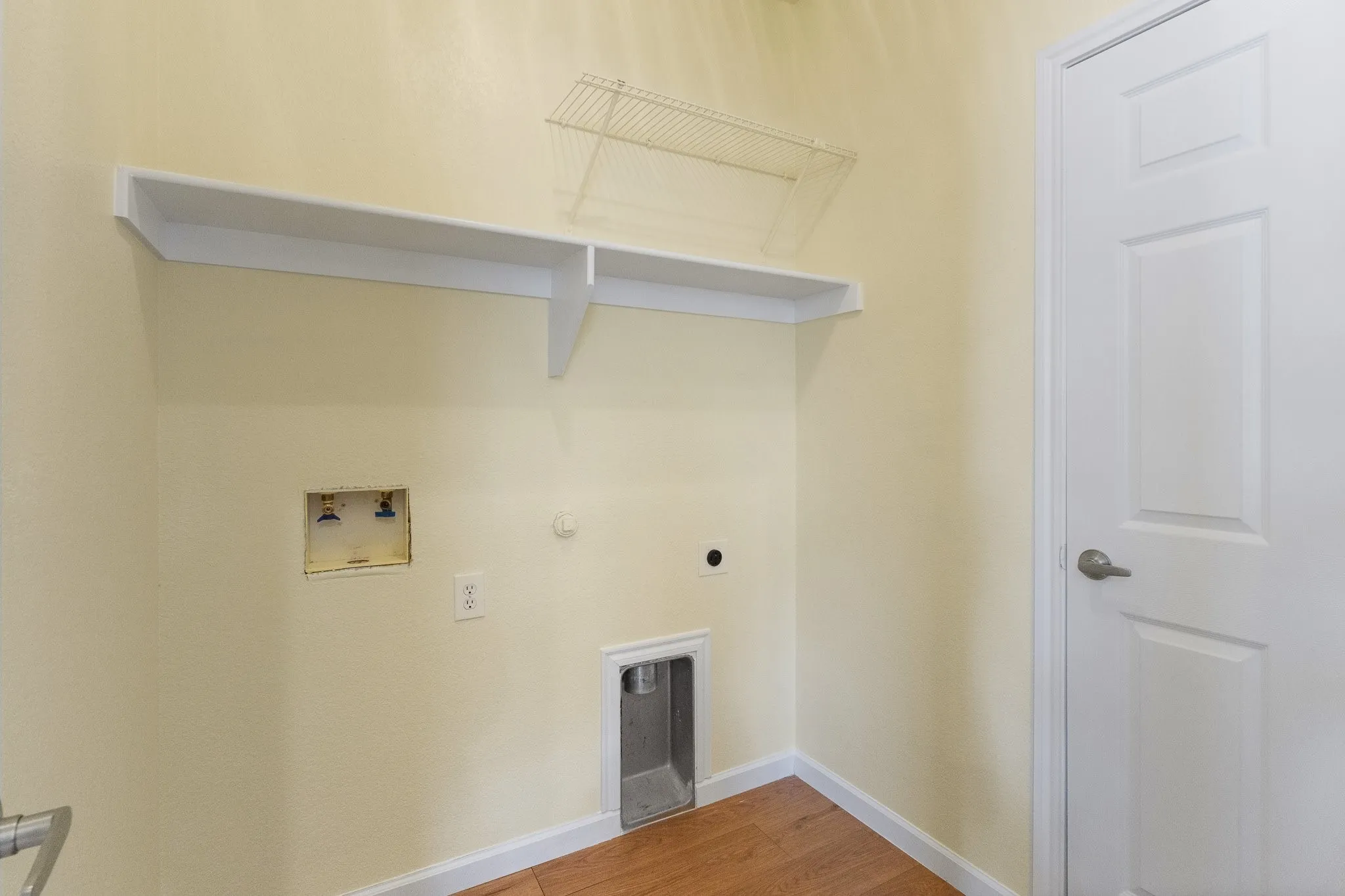 Laundry area featuring a built-in shelf, wire rack storage, wood-finish flooring, and a paneled door