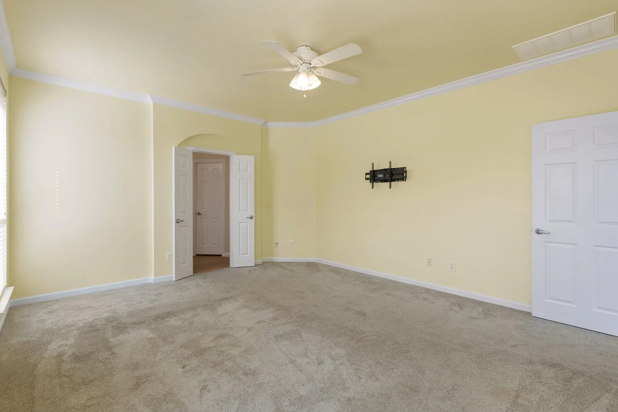 Carpeted room featuring a ceiling fan, crown molding, and an arched doorway