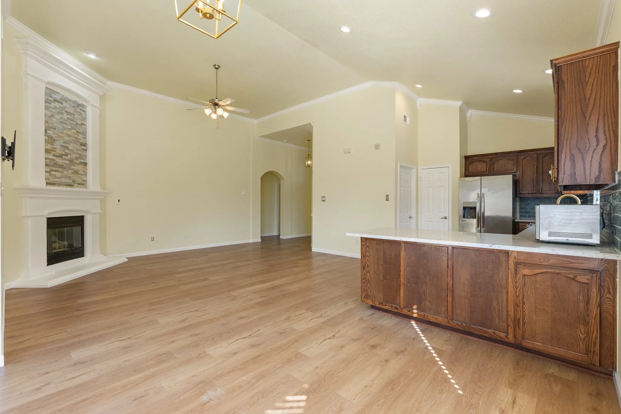 Wood-finish flooring throughout, featuring a corner fireplace with stone-look surround, a decorative crown molding, and an arched entryway