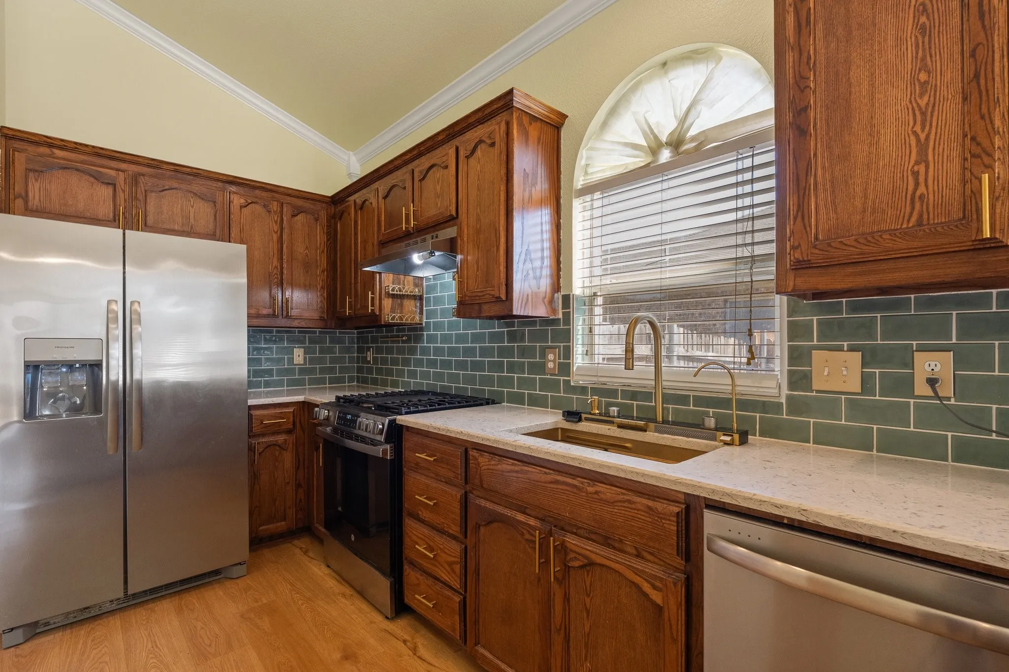 Kitchen featuring wood cabinetry, stainless steel appliances, a tile backsplash, light-toned countertops, and wood-finish flooring