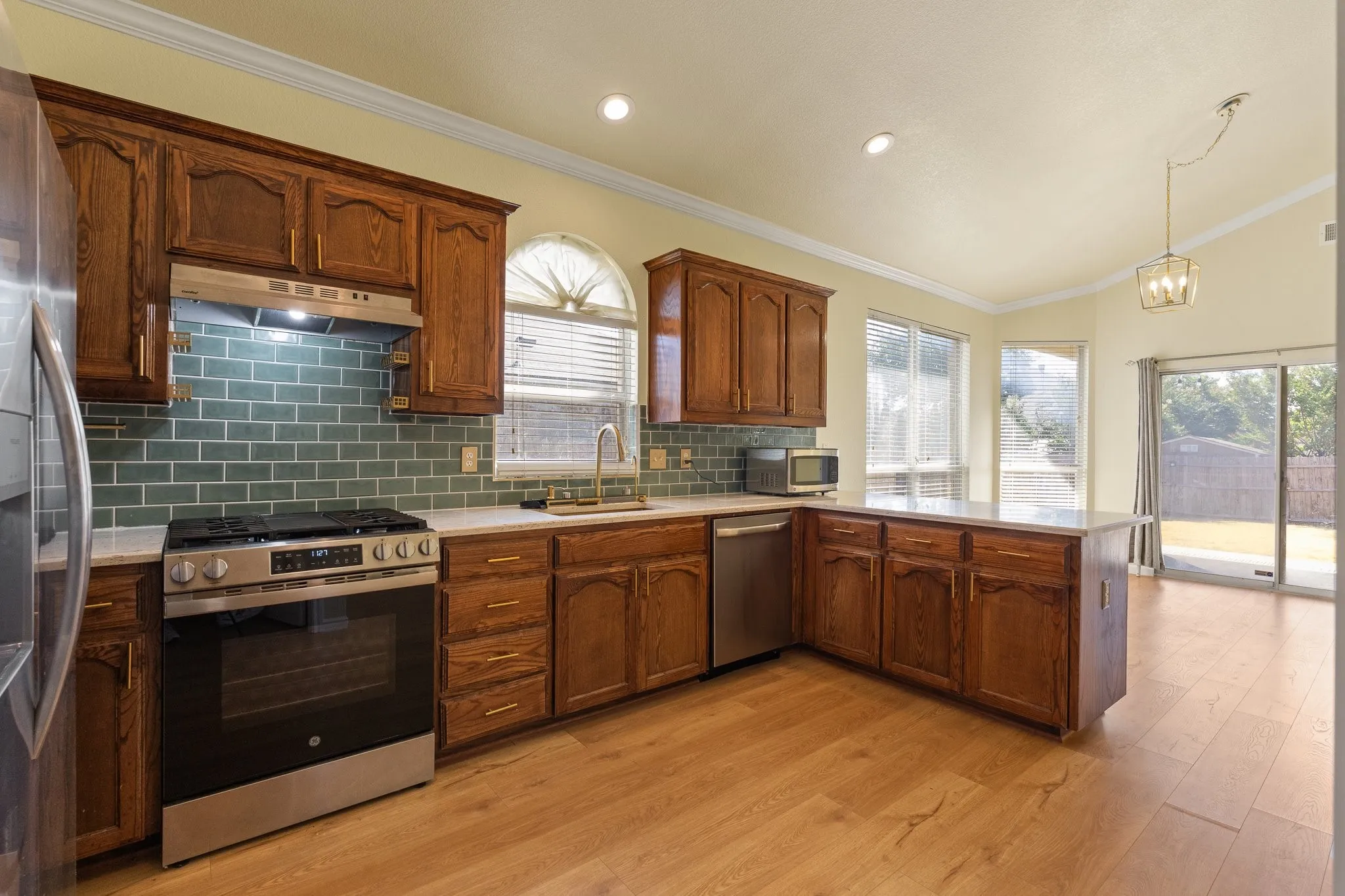 Kitchen featuring wood-finish flooring, stainless steel appliances, a tile backsplash, wood cabinetry, and a countertop island