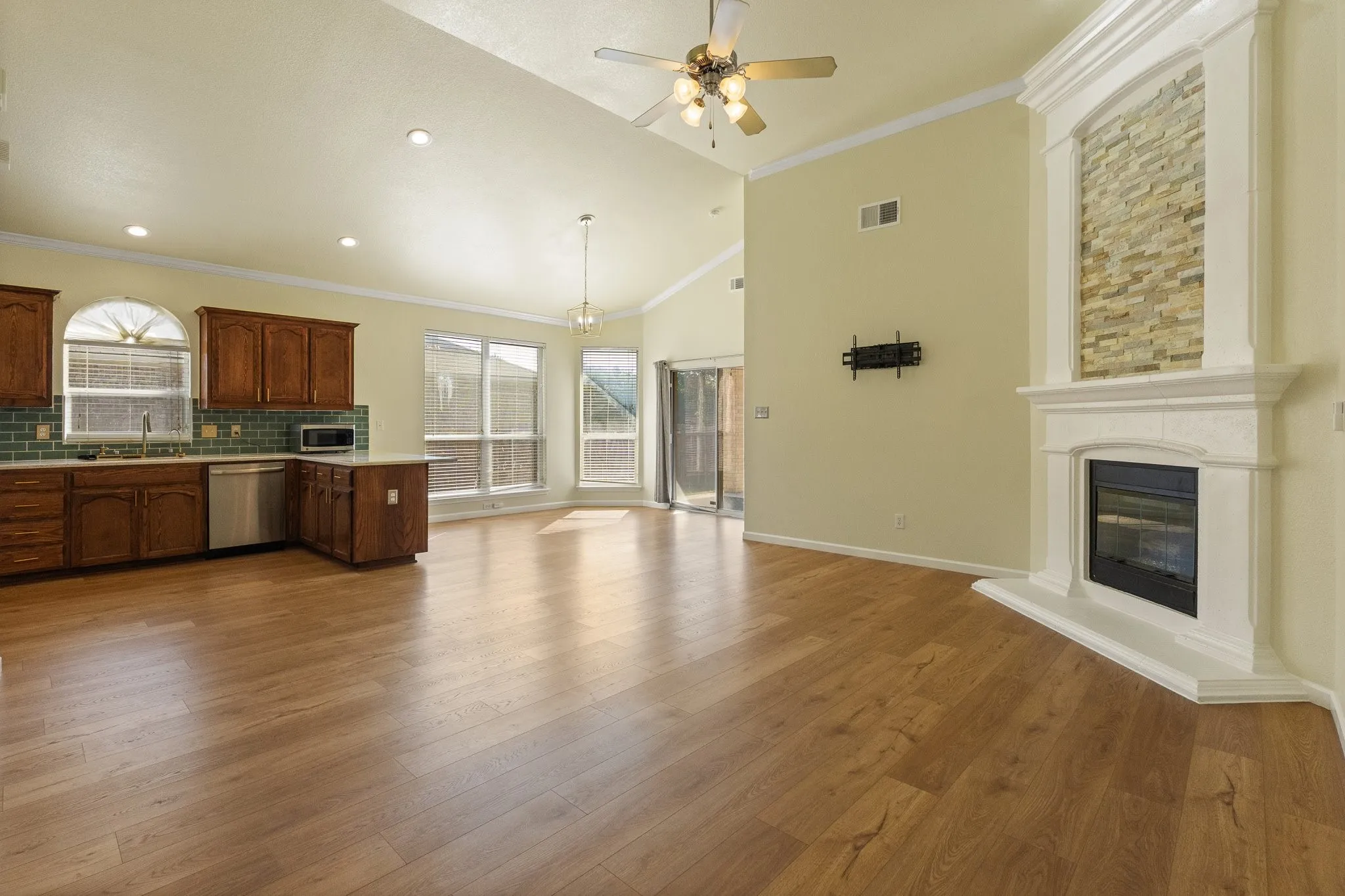 Open concept living area with wood-finish flooring, vaulted ceiling, and a fireplace featuring a stone-clad accent wall