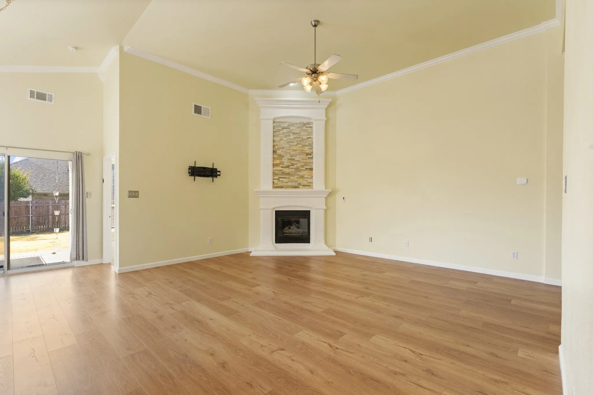 Wood-finish flooring throughout, vaulted ceiling, corner fireplace with stone-finish surround, ceiling fan, and sliding glass door to the exterior