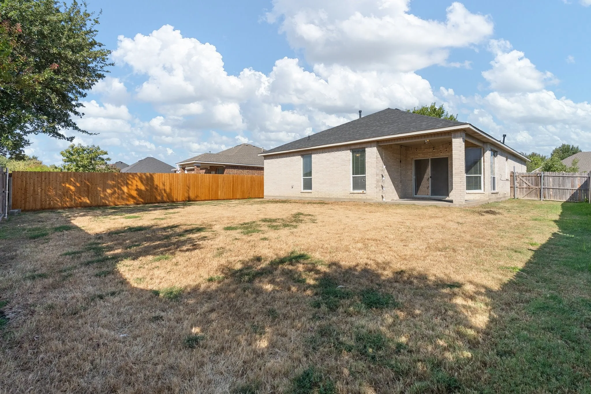 Expansive backyard featuring a wood privacy fence, a covered patio, and a light brick exterior