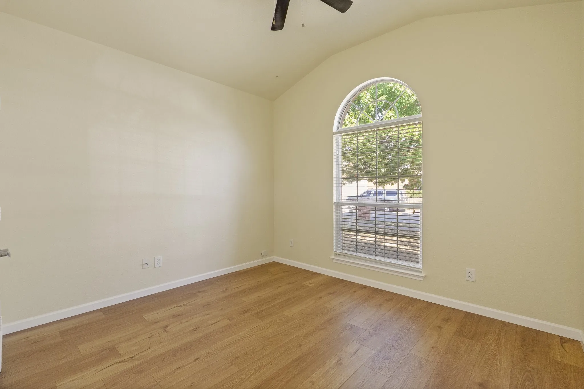 Vaulted ceiling with a ceiling fan, wood-finish flooring, and an arched window