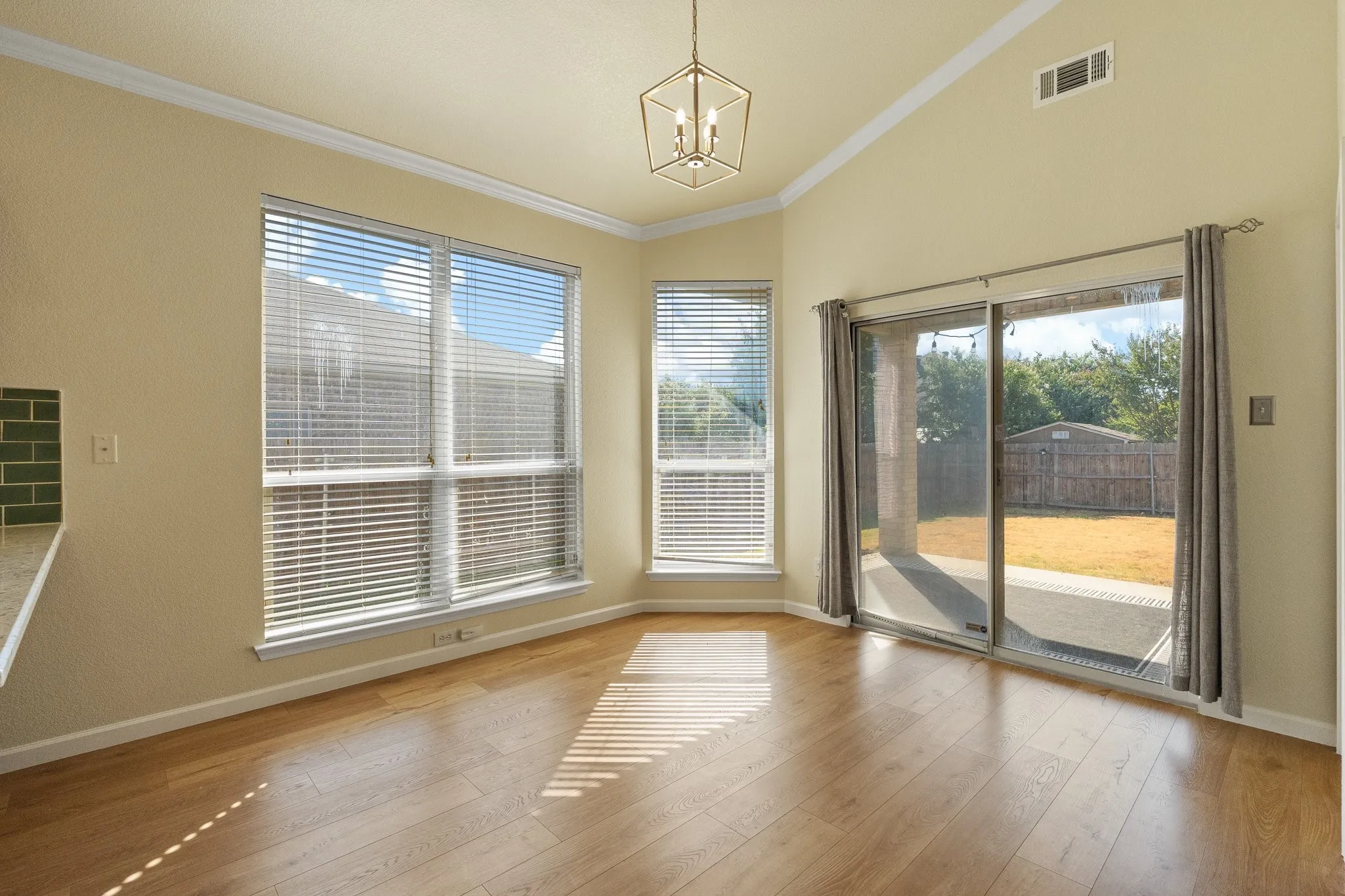 Vaulted ceilings, wood-finish flooring, a contemporary geometric light fixture, and sliding glass doors leading to an outdoor patio