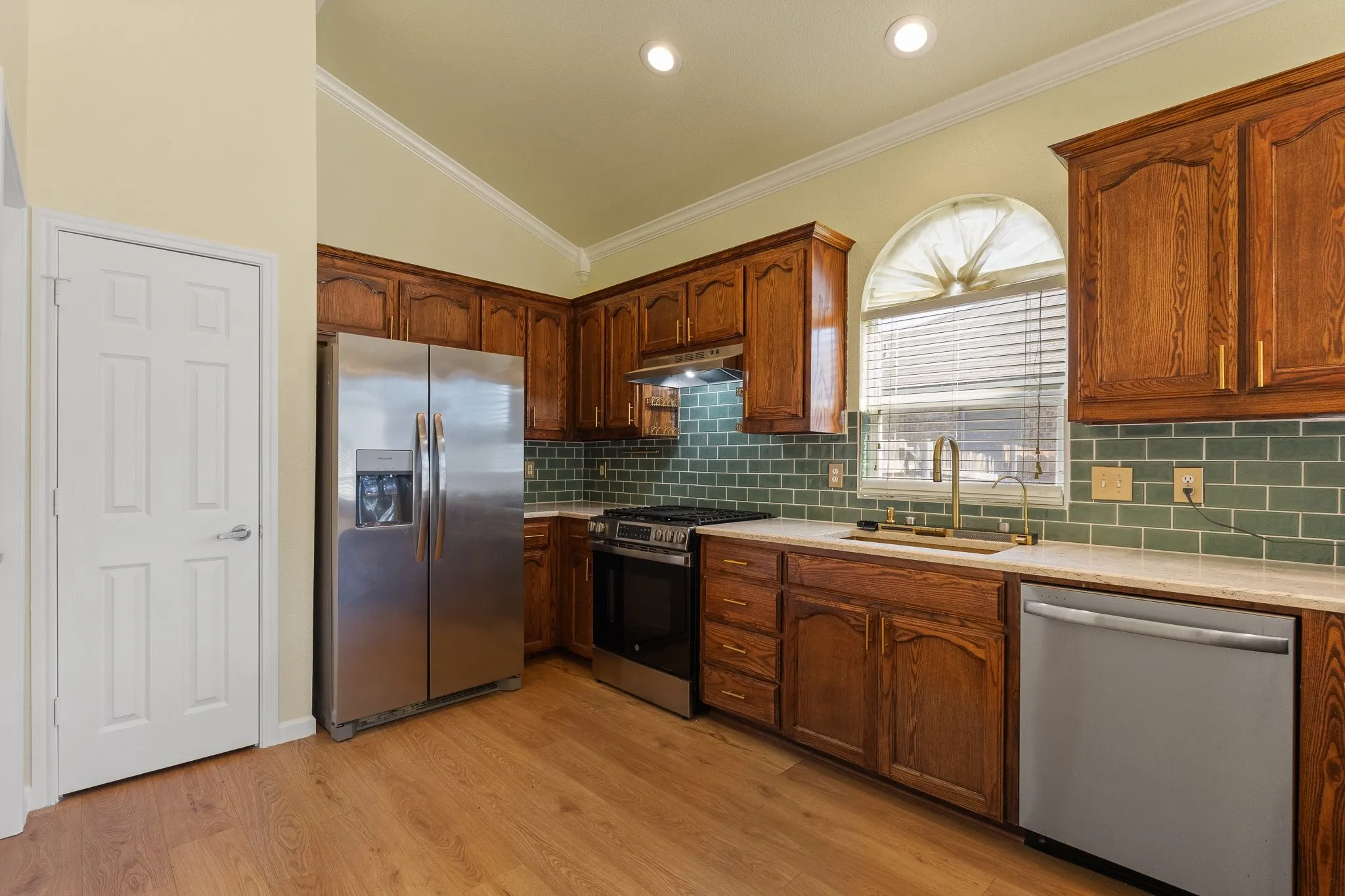 Wood-finish flooring, vaulted ceilings, recessed lighting, stainless steel appliances, and a tile backsplash