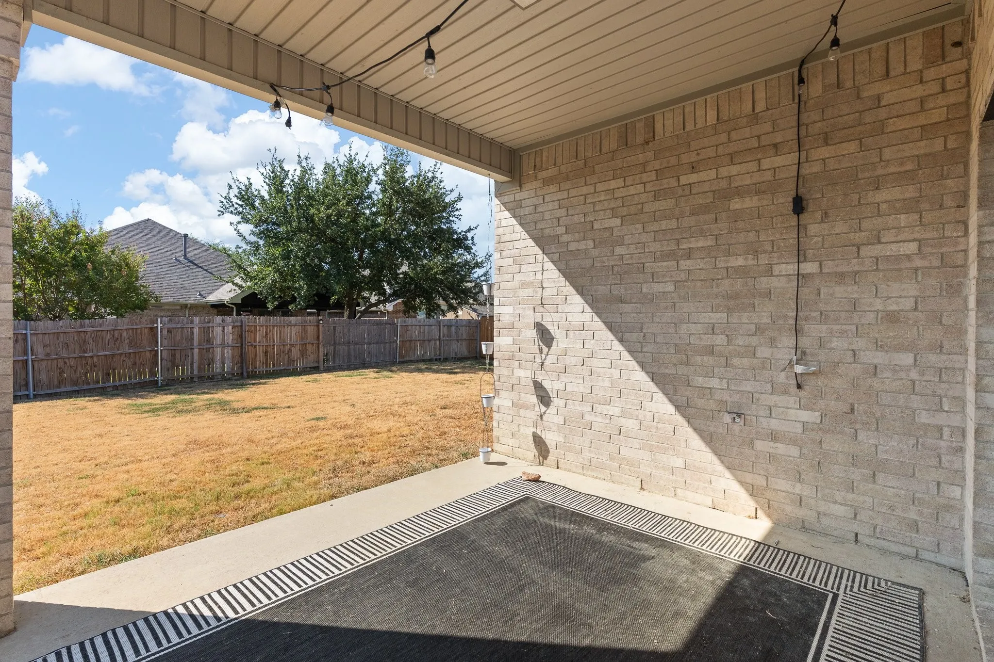 Covered patio with string lighting, brick exterior wall, and concrete flooring