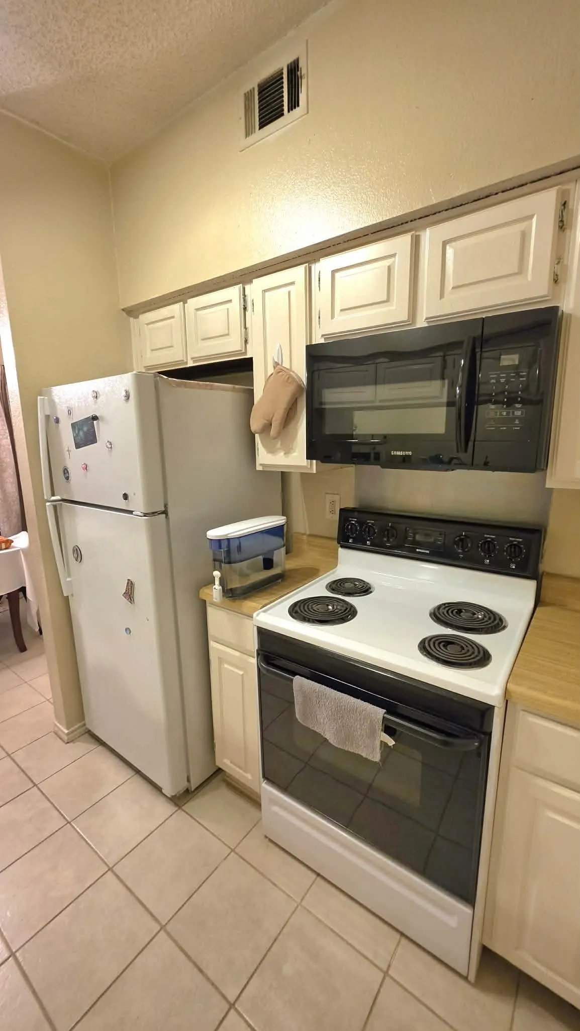 Kitchen featuring white cabinetry, a black over-the-range microwave, a white electric range, and light-toned tile flooring