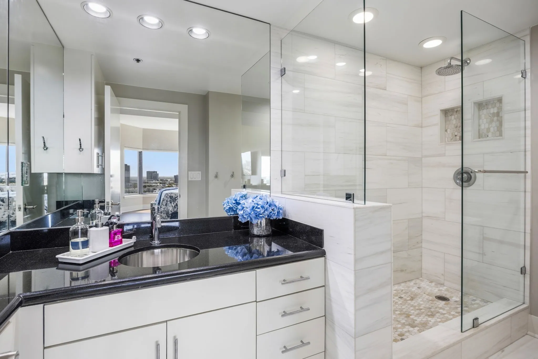 The completely renovated primary bath features a spacious walk-in shower with designer tile, a rain-shower-style showerhead, and a distinctive river-rock shower floor for a spa-inspired feel.