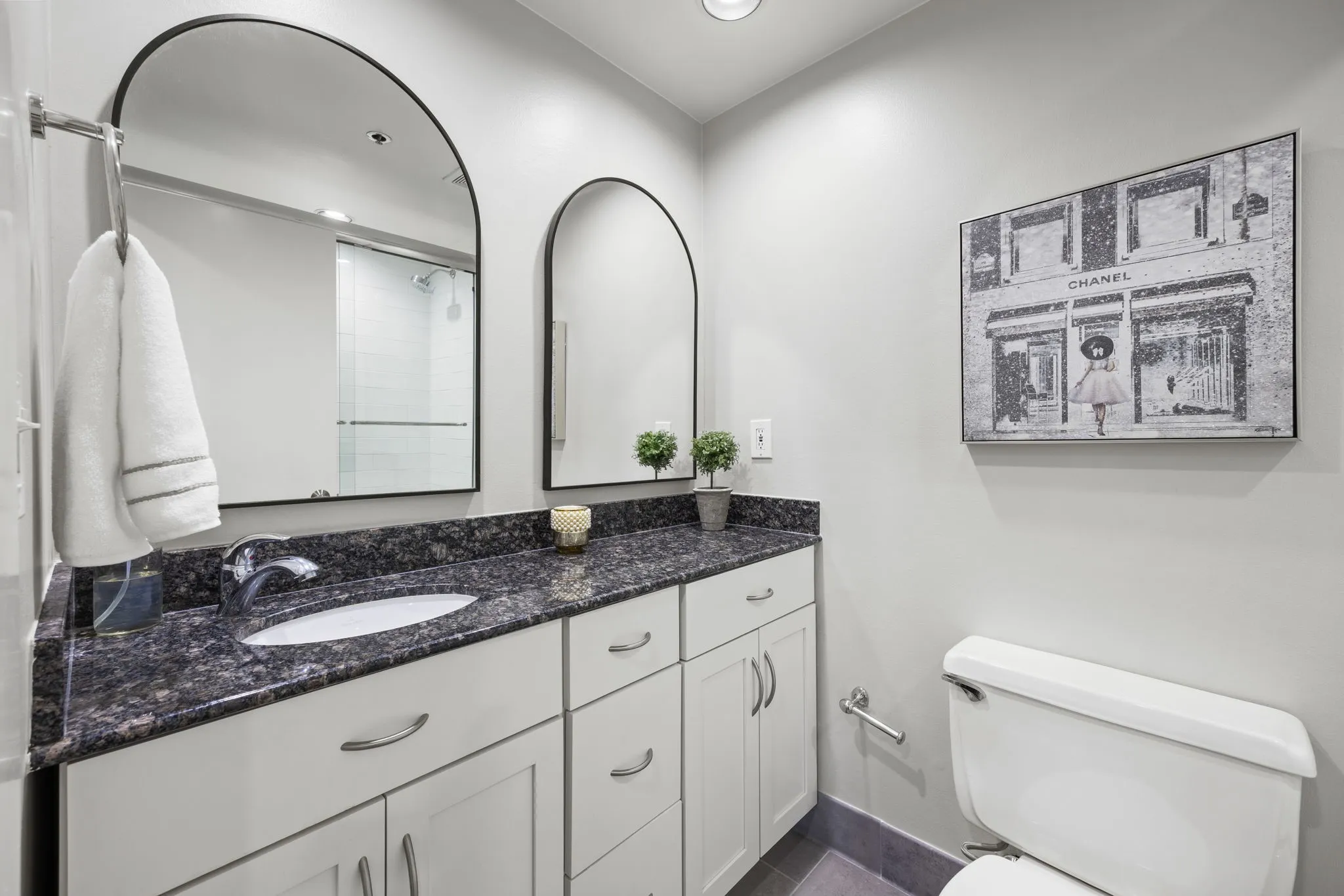 The beautifully updated guest bathroom features rich dark granite countertops, framed mirrors, stylish decorative lighting, and a tub-shower combination accented by a designer tile surround.