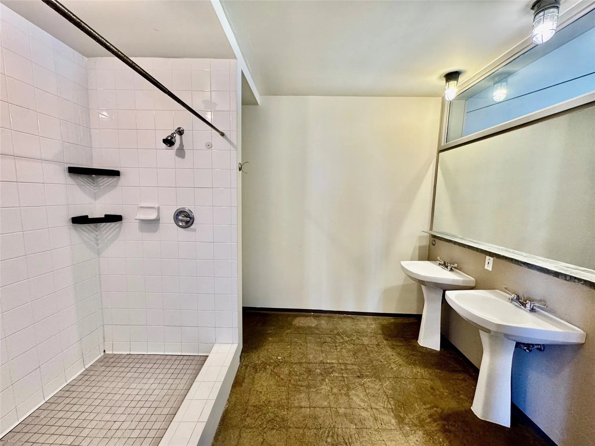 White tile shower with integrated shelving, two pedestal sinks, and concrete flooring
