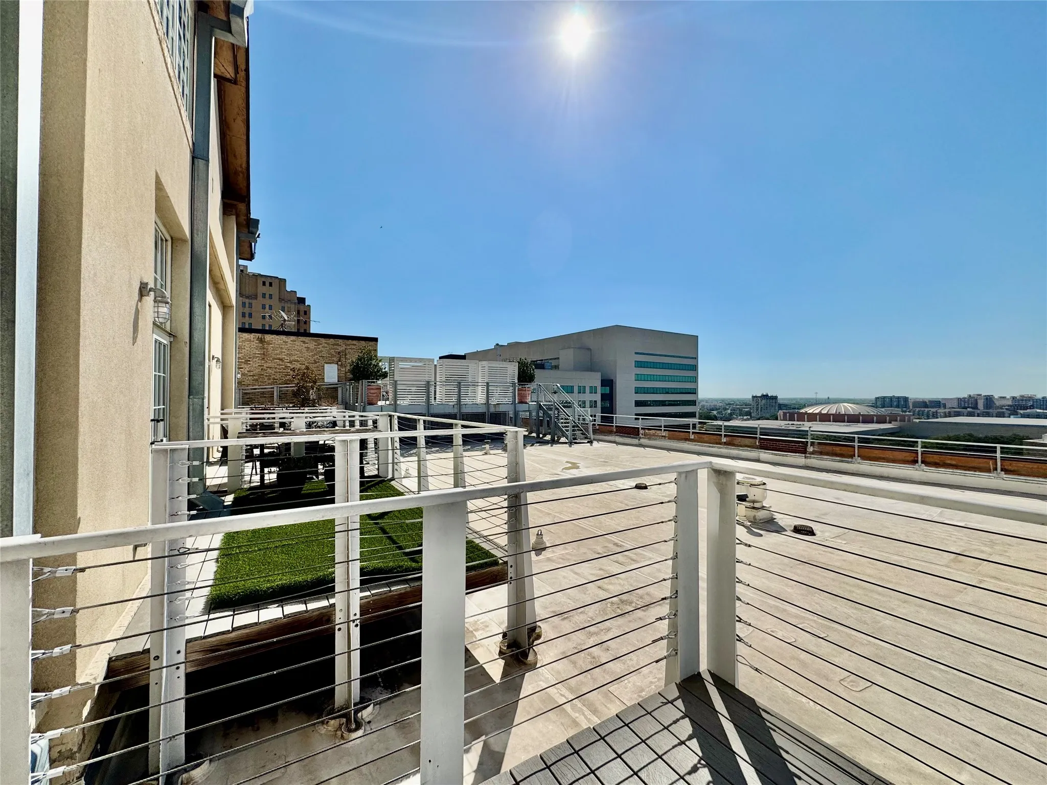 Expansive rooftop deck featuring a wood-finish surface, modern cable railing, and artificial turf sections