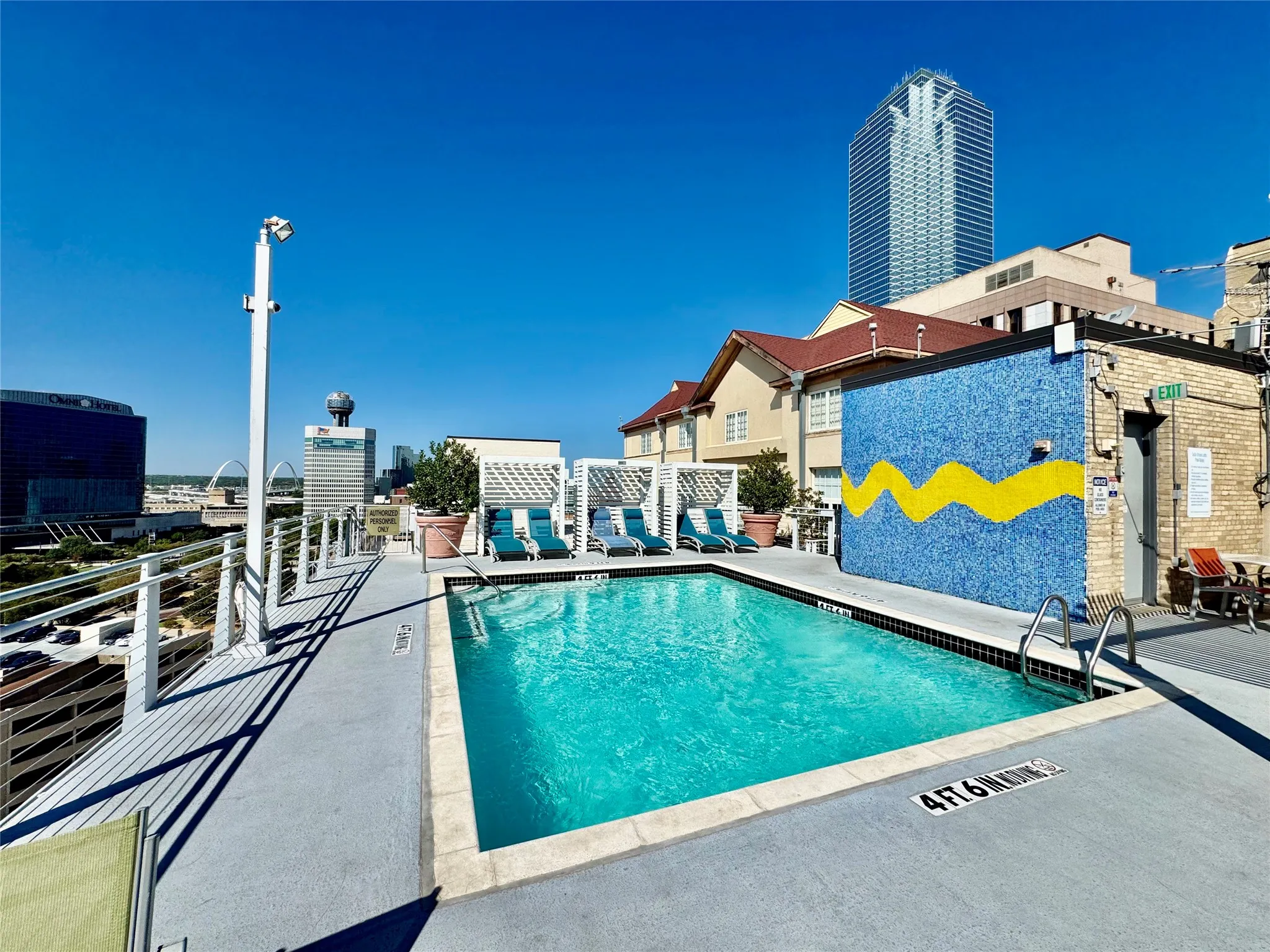 Rooftop swimming pool with city backdrop, featuring a mosaic-tiled accent wall, perimeter railings, and multiple cabanas