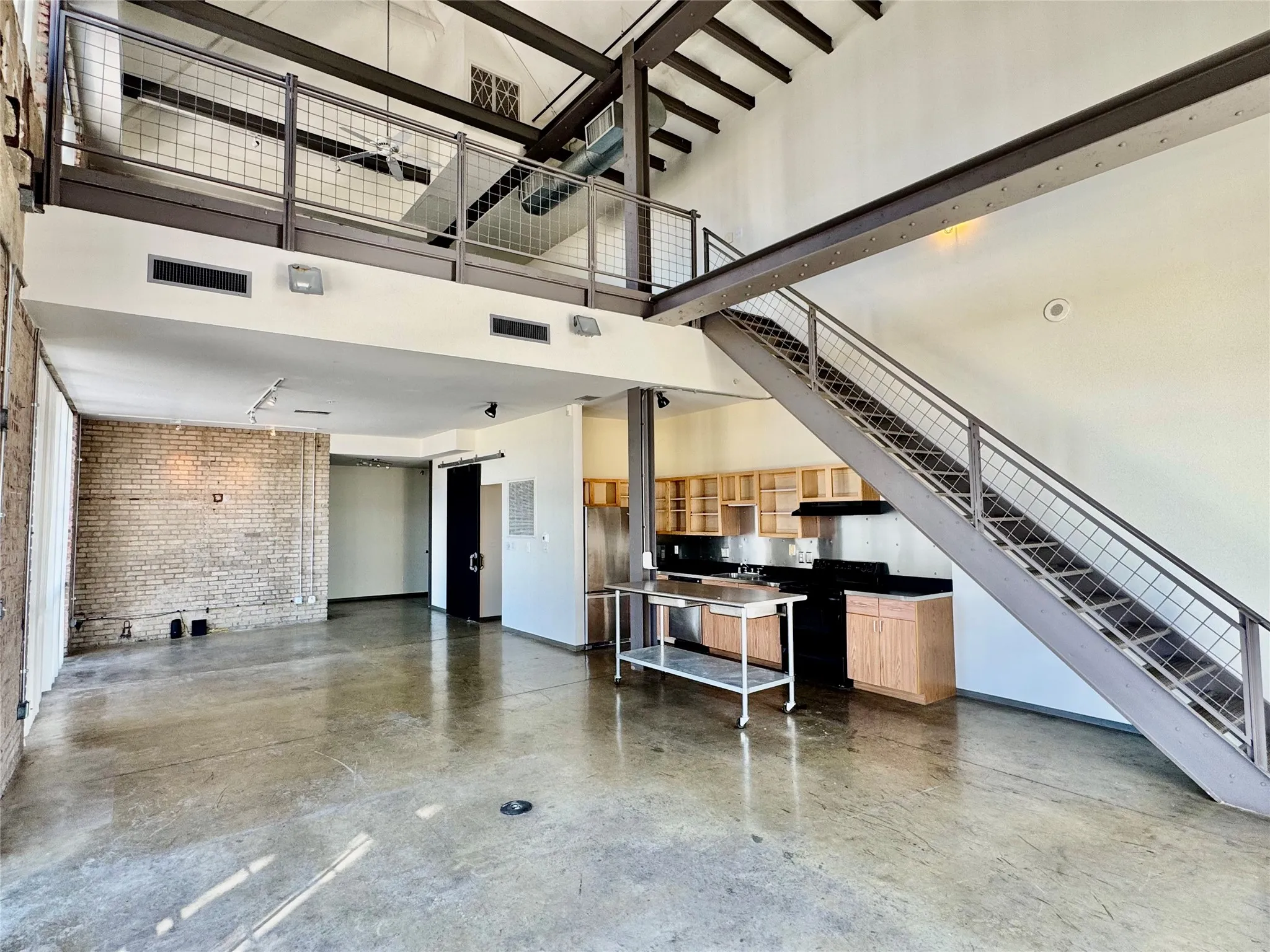 Polished concrete flooring, exposed brick accent wall, open-tread staircase with metal railing, mezzanine level with metal railing, and exposed structural beams