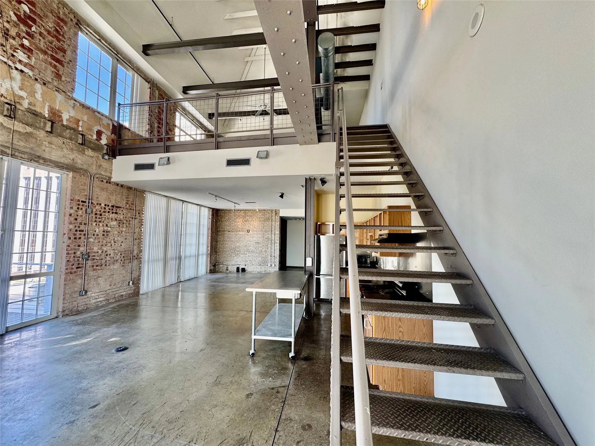 Exposed brick walls, concrete flooring, industrial metal staircase, and an upper-level mezzanine