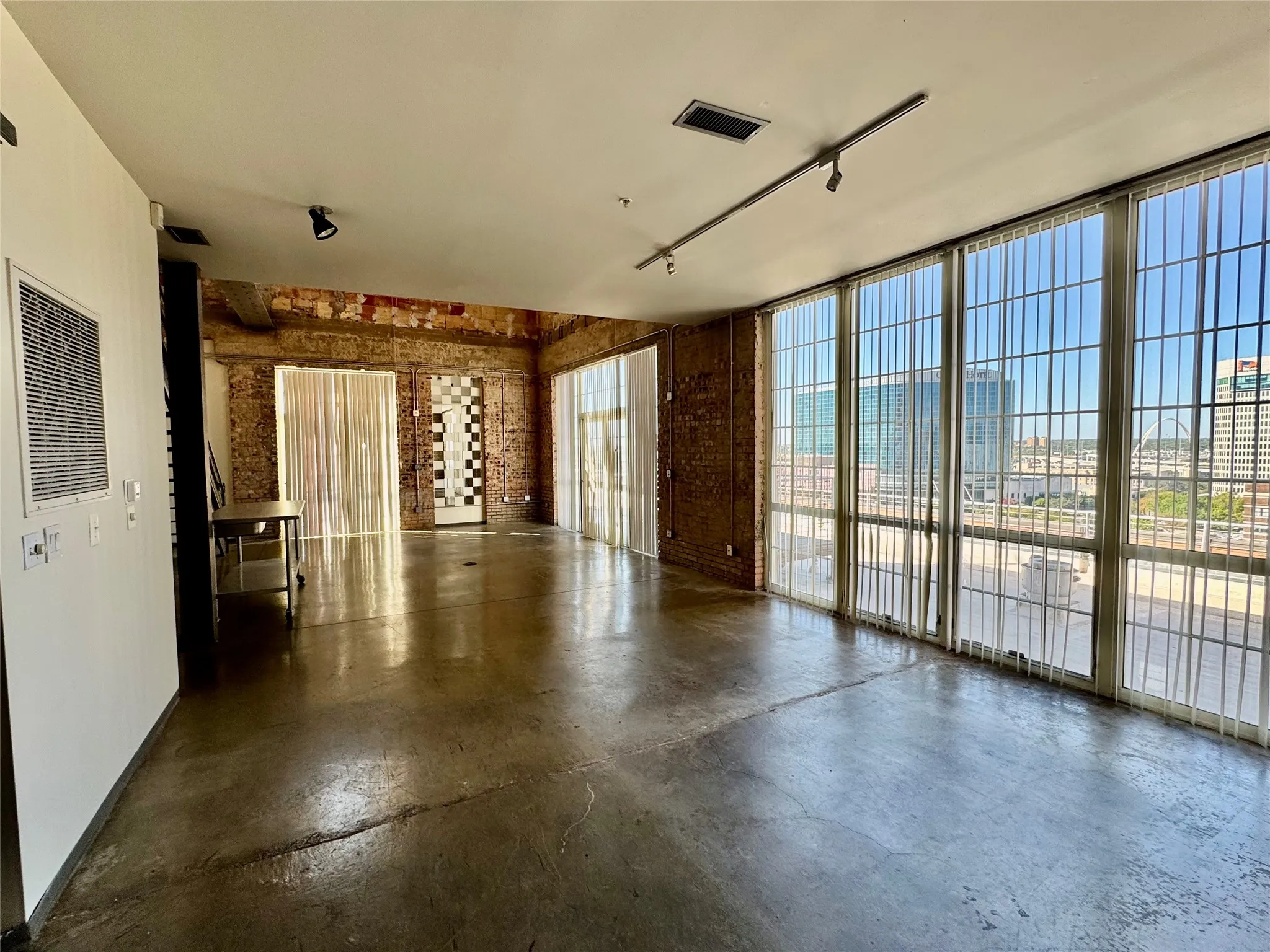 Polished concrete flooring, exposed brick wall accents, expansive window wall, track lighting, and high ceilings