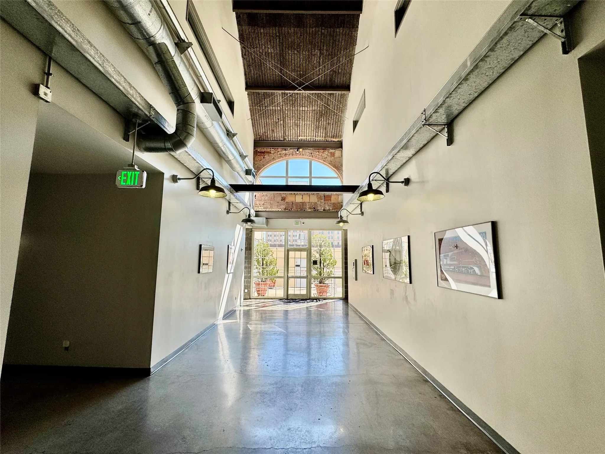 Polished concrete flooring, exposed overhead ductwork, multiple wall-mounted sconce lights, and a full-light glass entry door with transom window