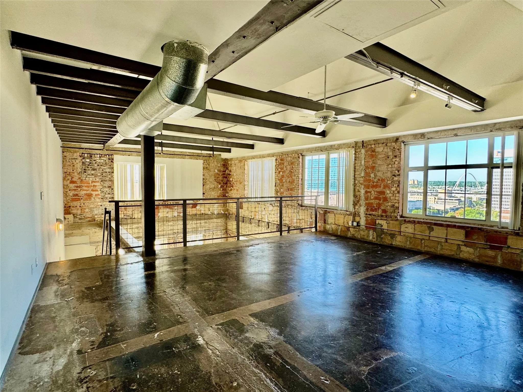 Exposed brick walls, wood-finish ceiling beams, concrete flooring, large windows, and an open concept upper level with a metal railing