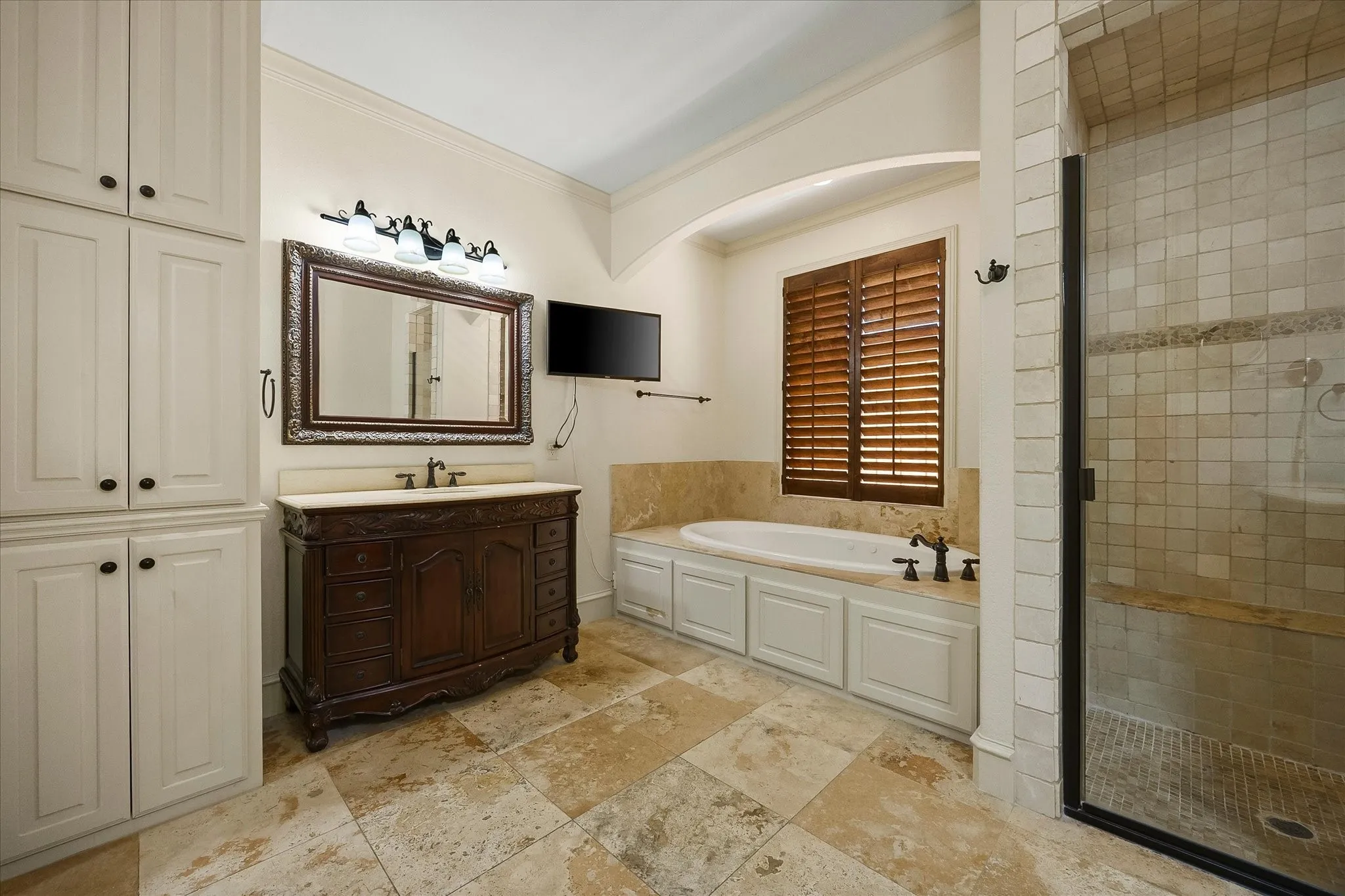 Built-in soaking tub, separate shower with tiled bench, ornate wood vanity with stone countertop, extensive built-in cabinetry, and tile flooring
