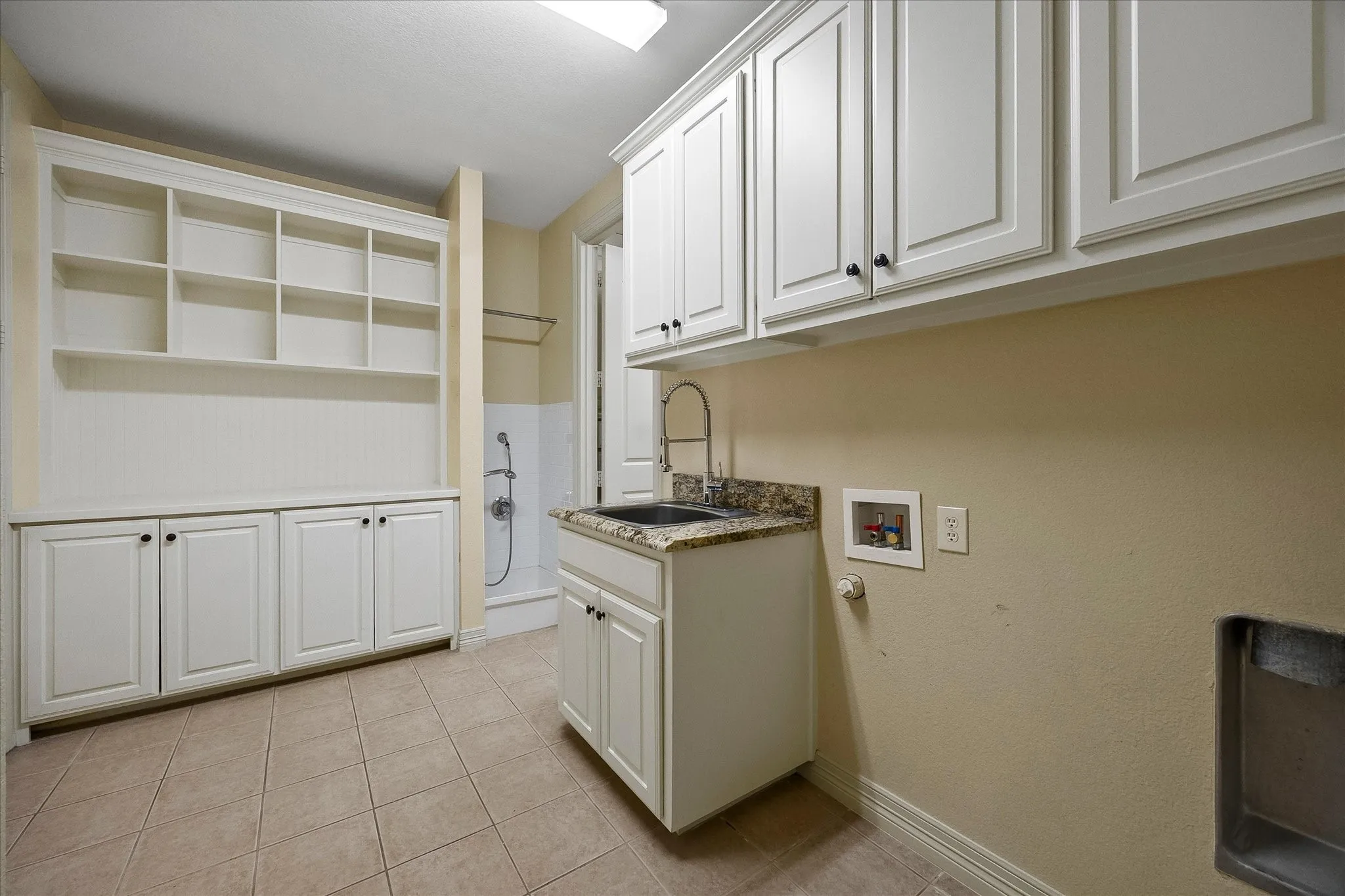 Built-in shelving, white cabinetry, tile flooring, utility sink with stone-finish countertop, and wall-mounted faucet