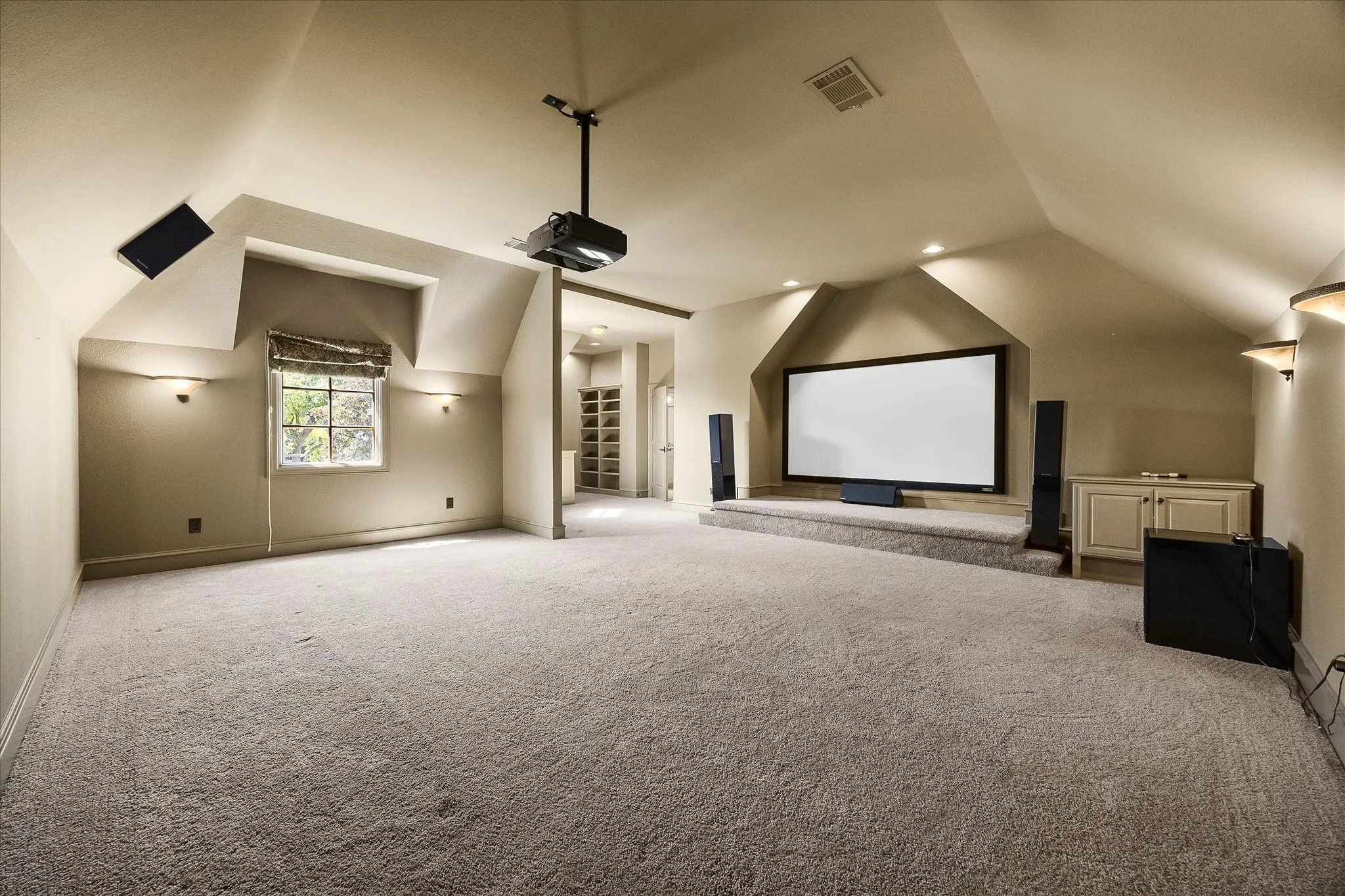 Carpeted room with a projector and screen, built-in cabinetry, and integrated wall sconces