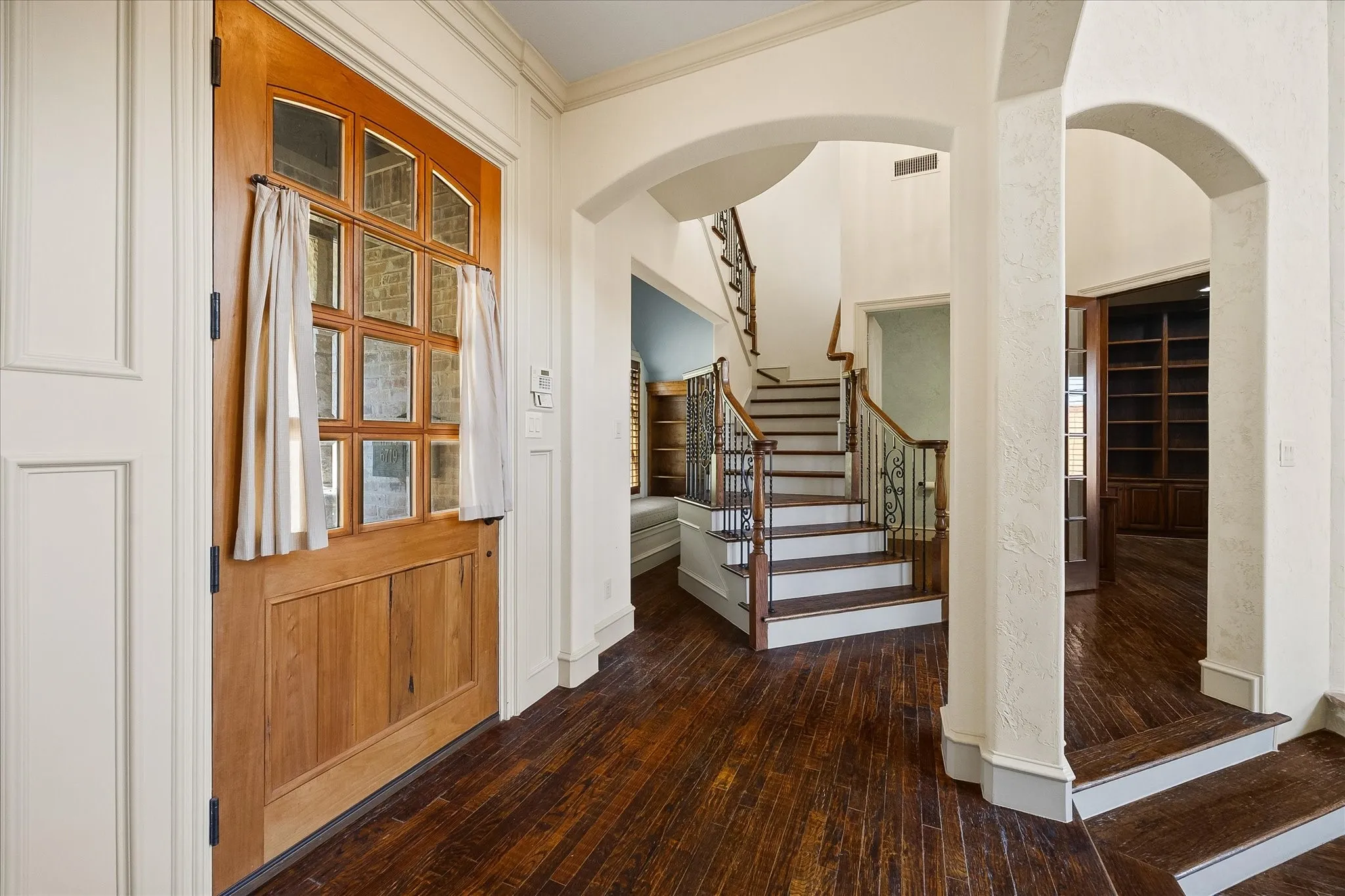 Hardwood flooring throughout the entry, staircase with wood treads and wrought iron balusters, arched doorways, and a wood entry door with divided lites
