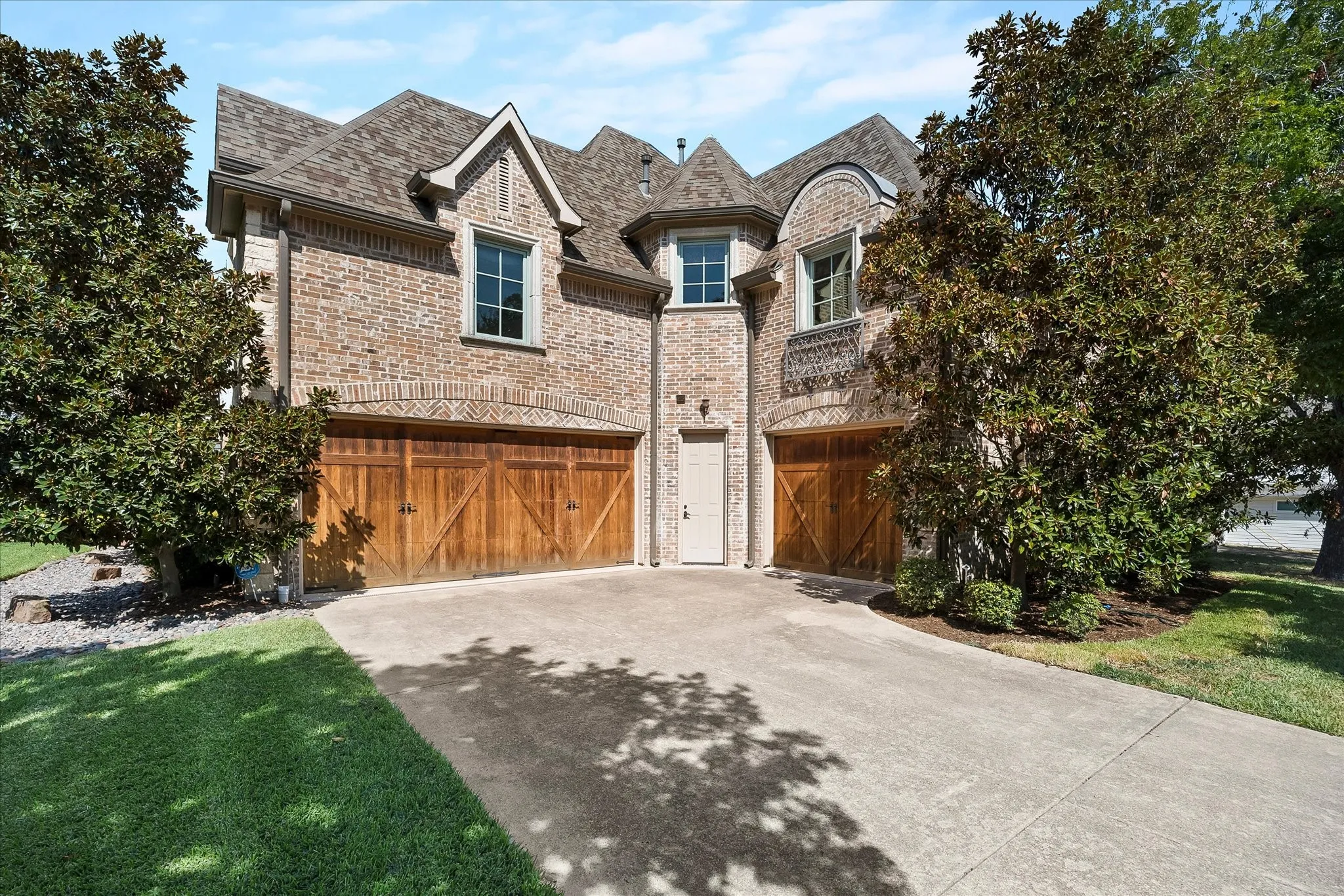 Brick exterior with a multi-gabled roofline, featuring two distinct wooden garage doors and a paved driveway
