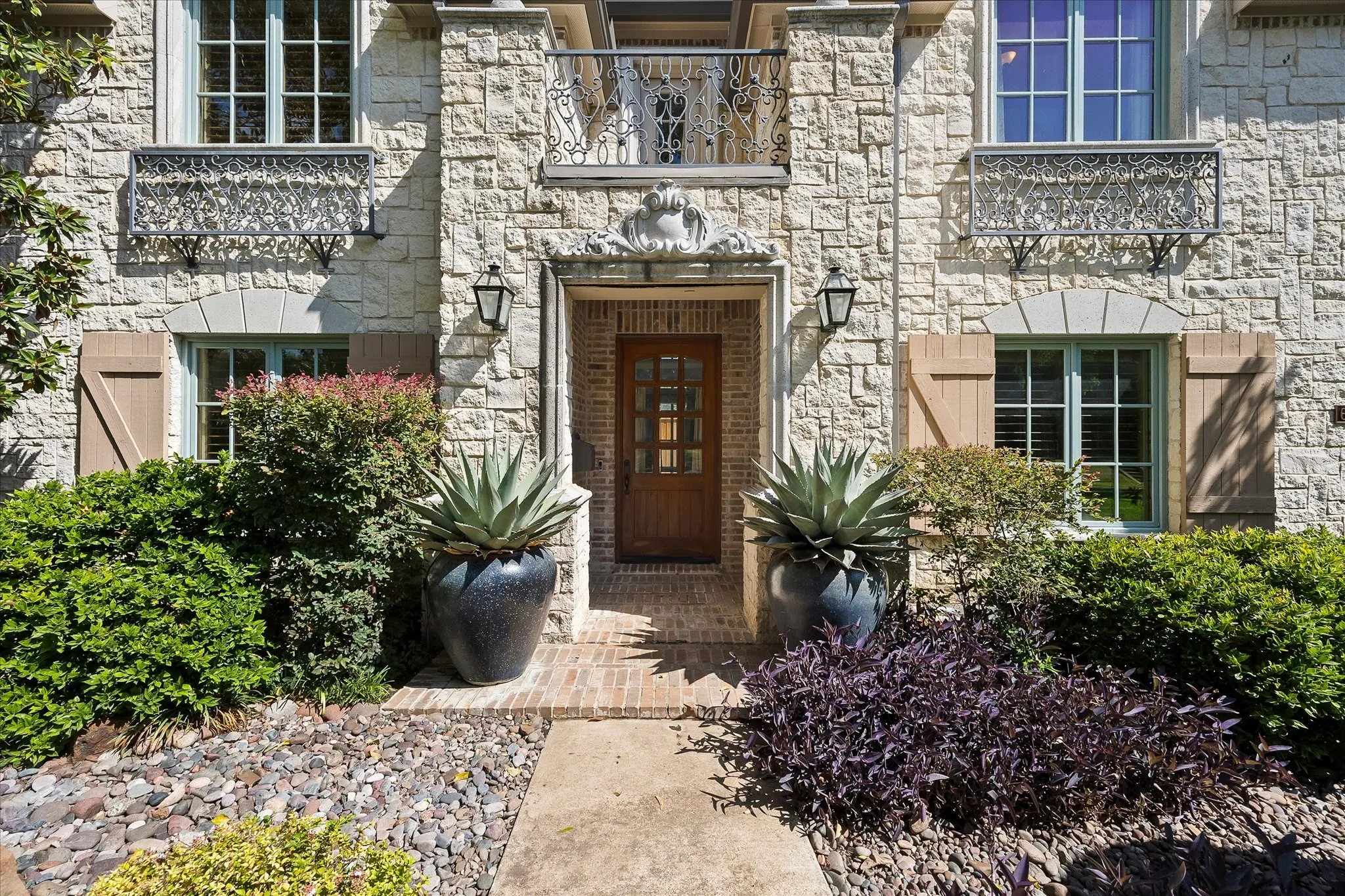 Stone exterior with decorative ironwork, arched window surrounds, wood shutters, and a wood entry door
