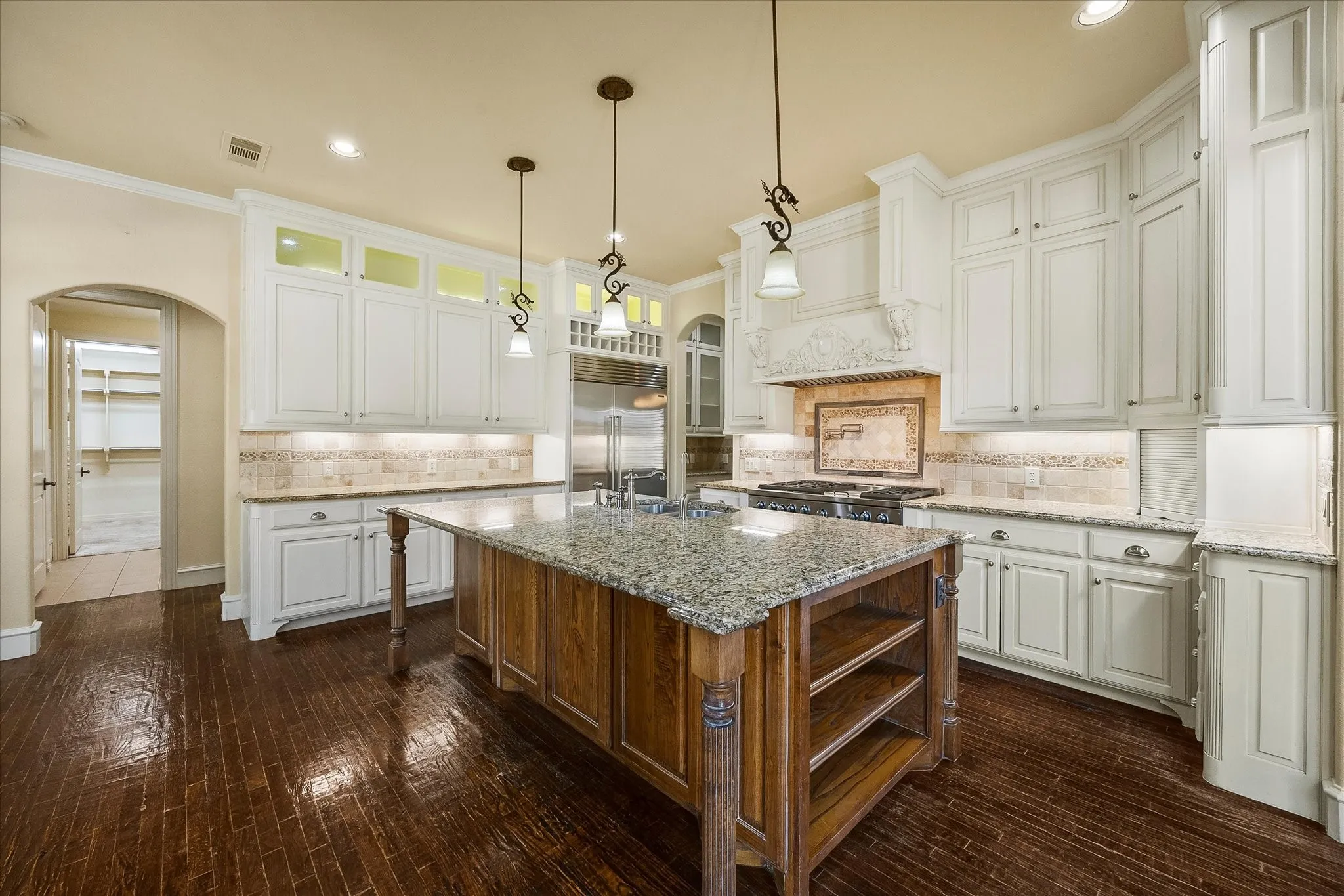 Kitchen featuring a wood-finish floor, white cabinetry, decorative range hood, granite countertops, and a wood-finish island with shelving