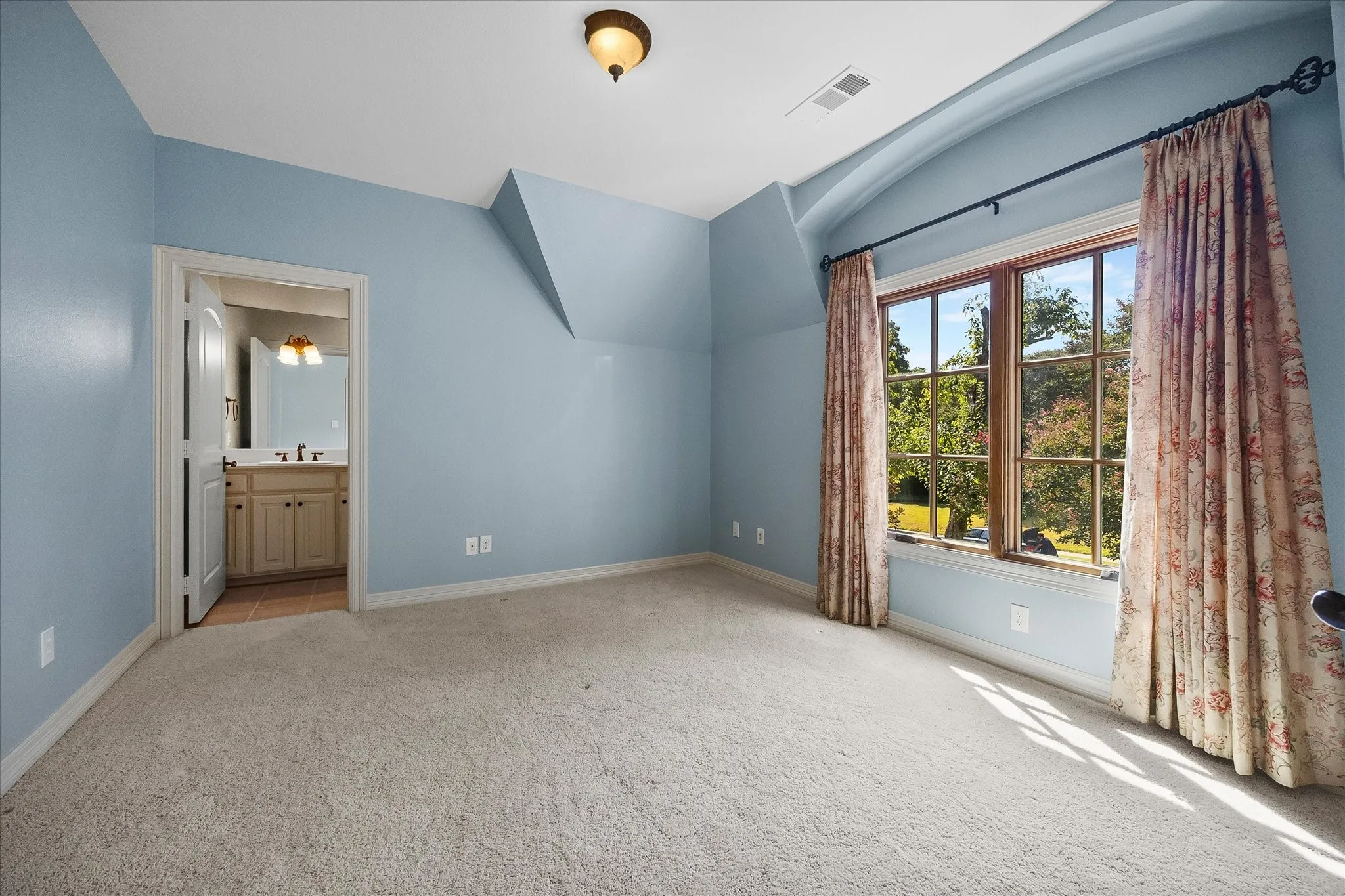 Carpeted room with a large multi-pane window, sloped ceilings, and an arched entryway leading to a bathroom featuring a vanity with a built-in sink