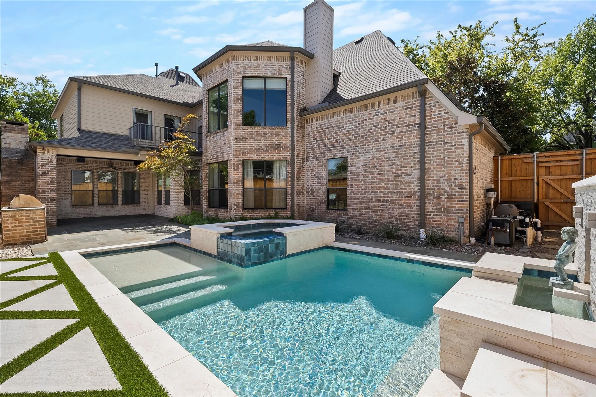 Brick exterior with multiple windows, covered patio, integrated pool and spa, and structured hardscaping