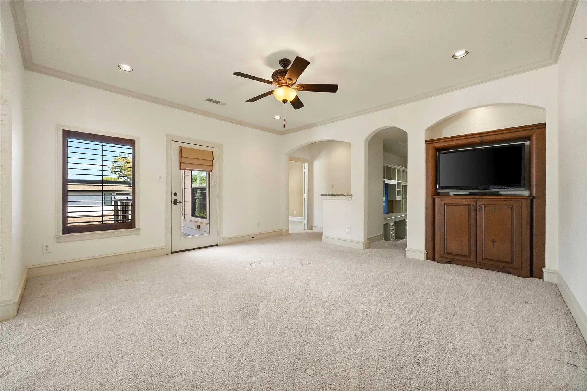 Recessed lighting, ceiling fan, arched doorways, built-in media cabinet, and a glass-paneled door