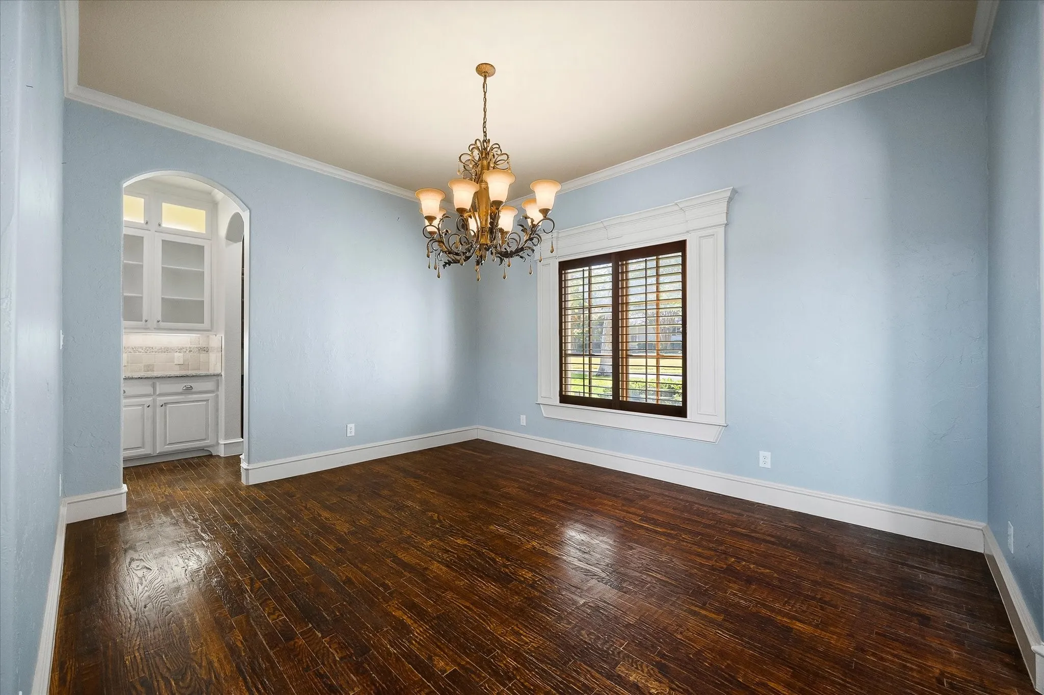 Wood-finish flooring, ornate chandelier, window with plantation shutters, crown molding, and built-in cabinetry with a countertop