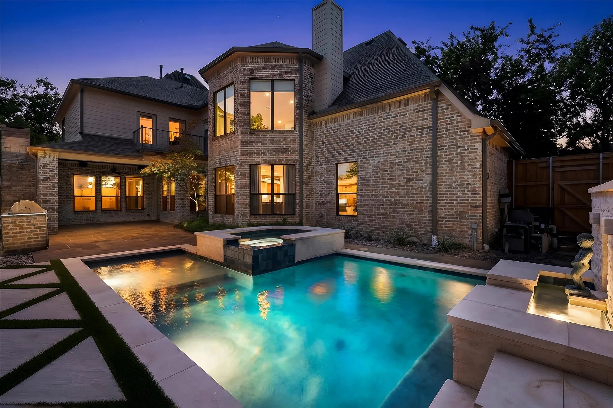 Brick exterior with dark trim windows, integrated swimming pool, attached spa, covered patio, and a stone water feature