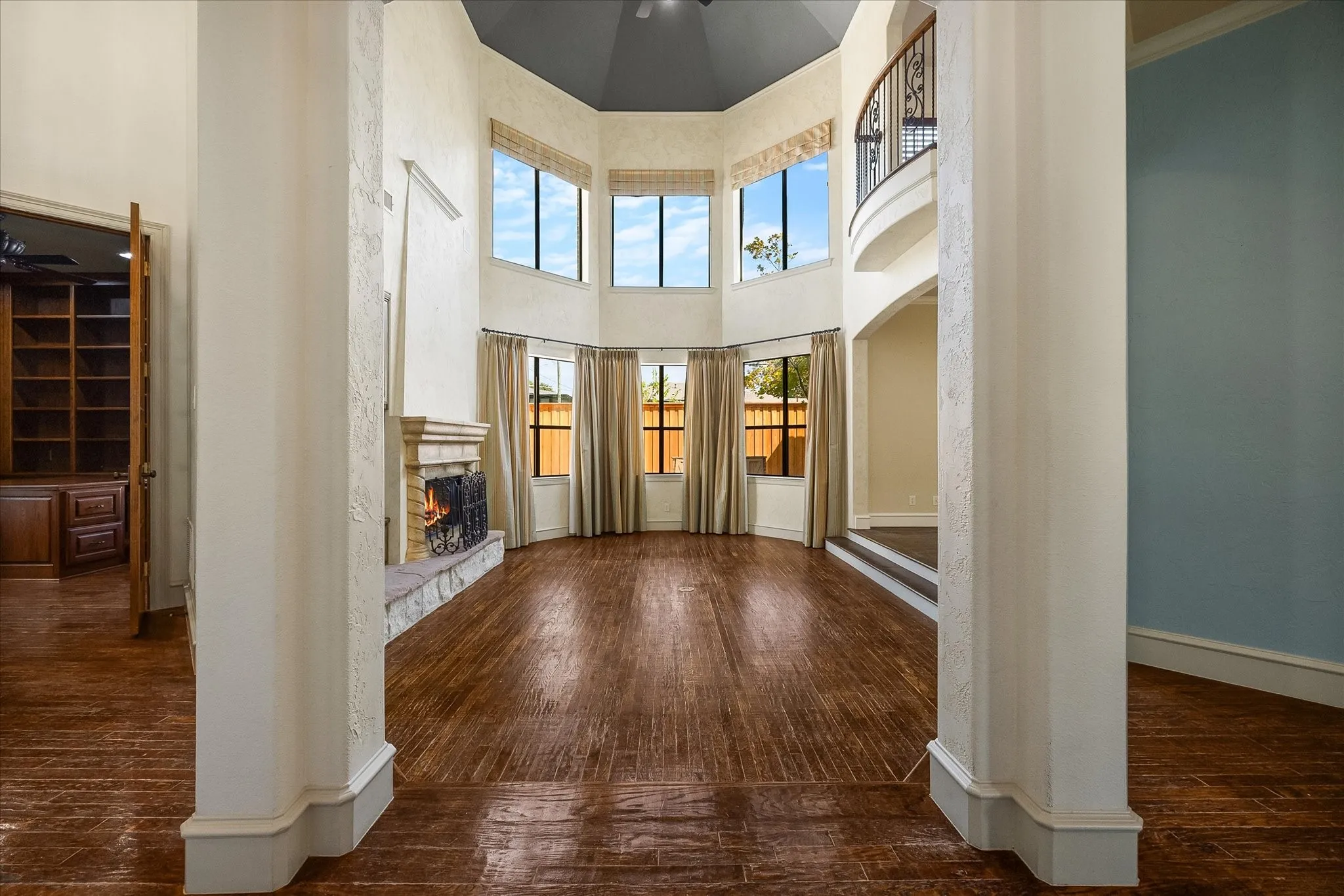 Two-story interior featuring wood-finish flooring, a stone fireplace, and a second-story interior balcony with an ornate railing