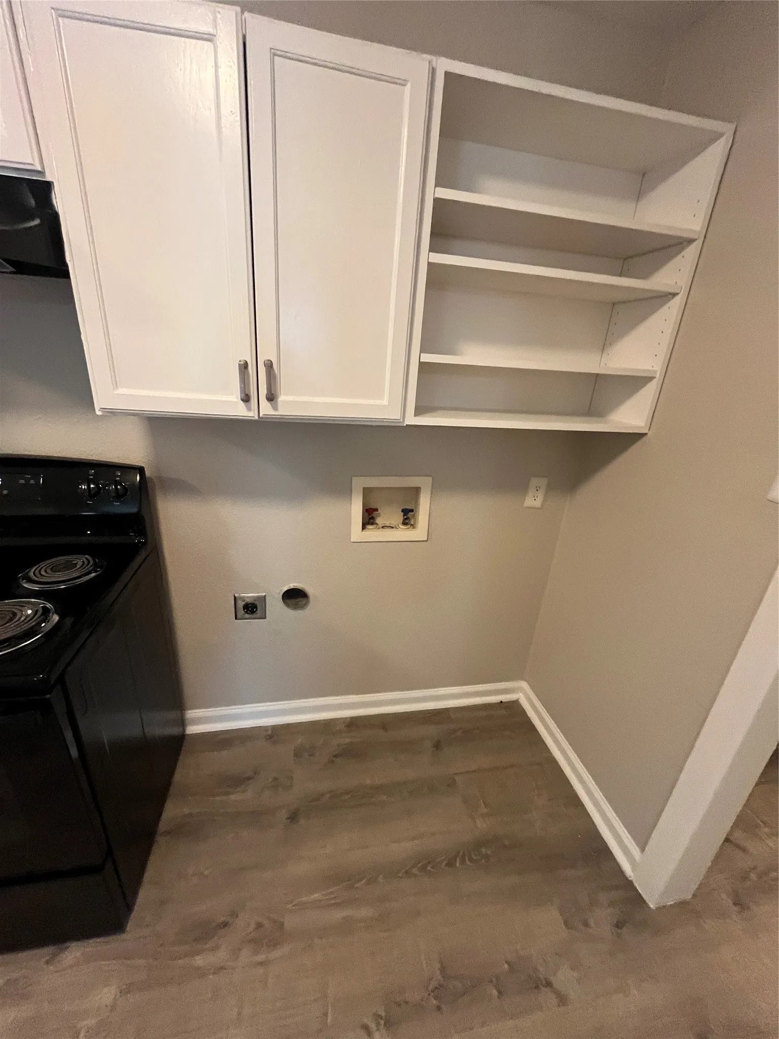 White cabinetry, open shelving, wood-finish flooring, and a laundry hookup