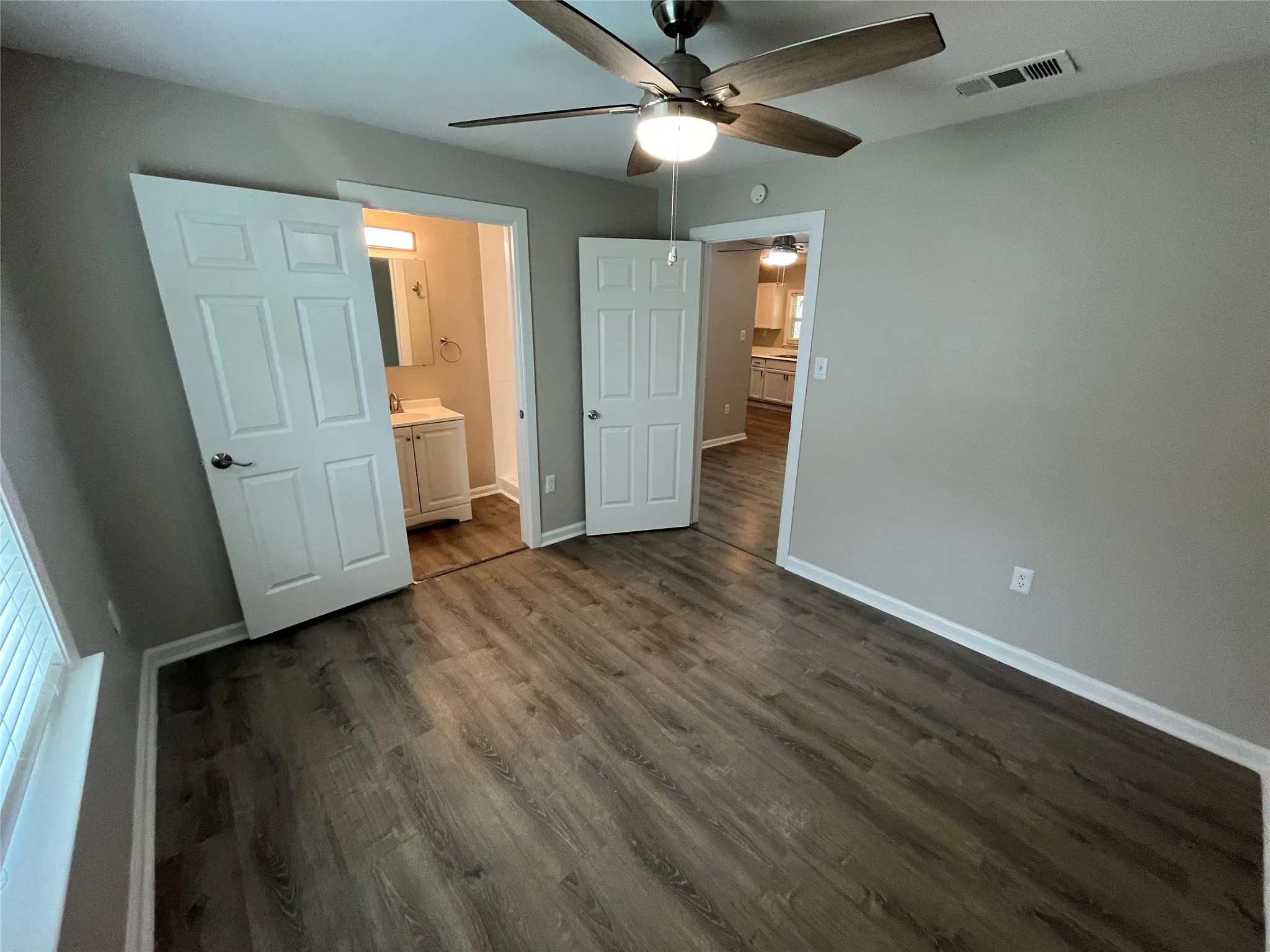 Wood-finish flooring throughout, ceiling fan with integrated lighting, and white paneled doors