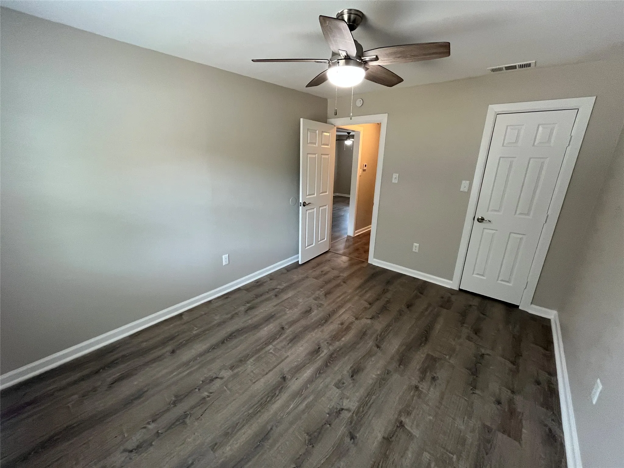 Wood-finish flooring, neutral wall tones, ceiling fan with integrated lighting, and white paneled doors