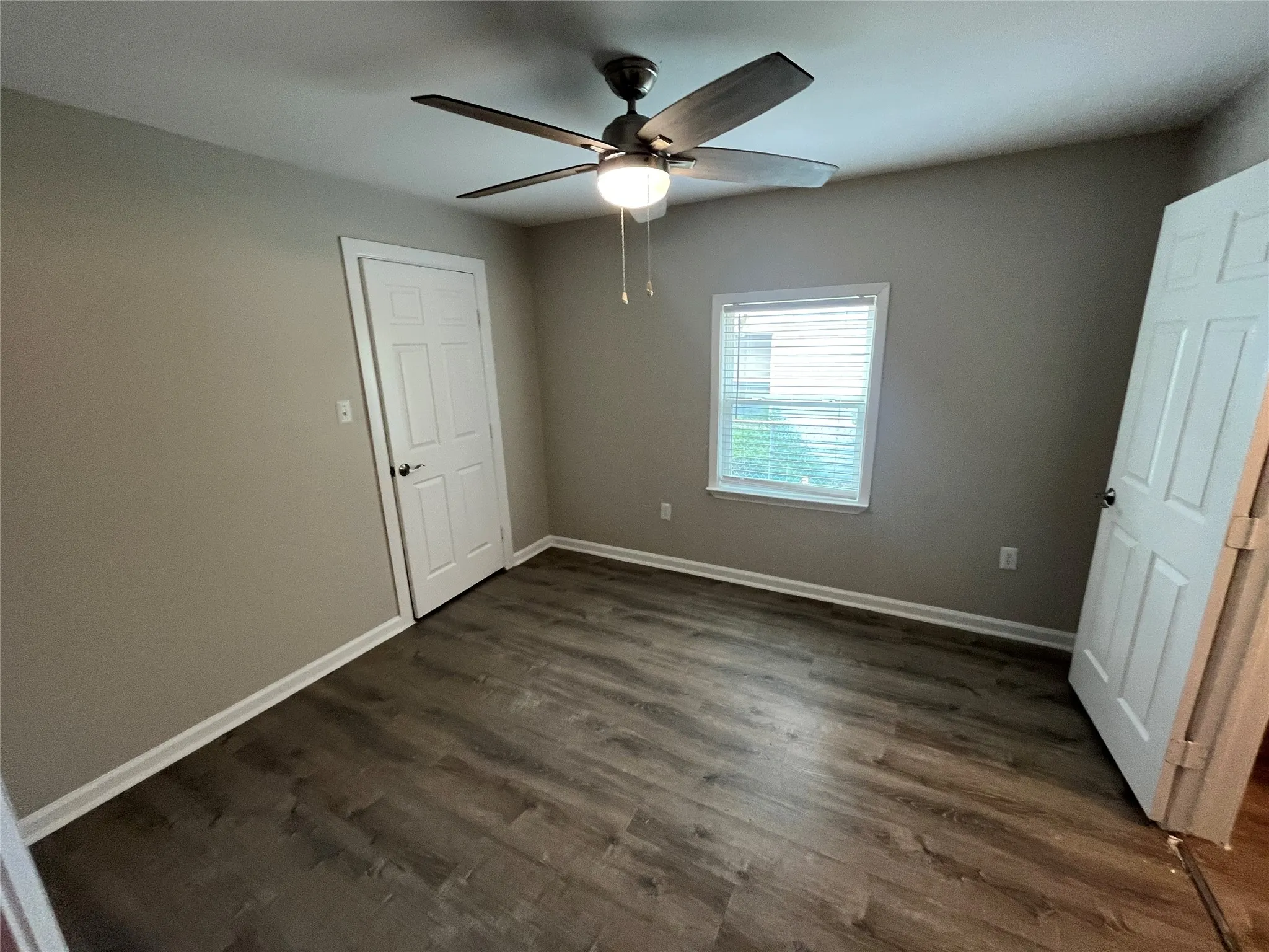 Wood-finish flooring with neutral wall tones, modern ceiling fan with integrated lighting, and a window with blinds