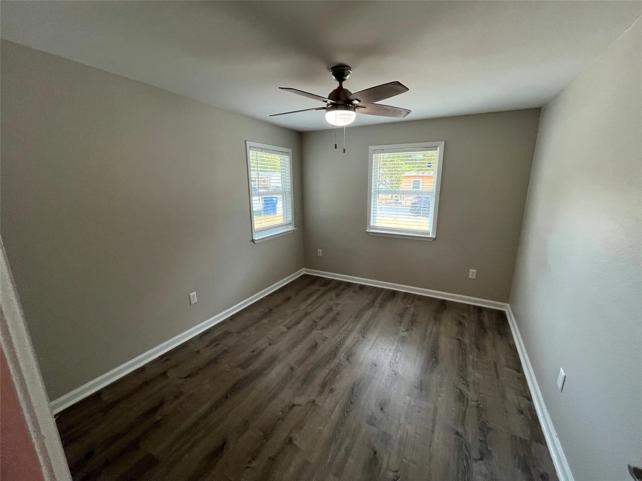 Wood-finish flooring, two windows with blinds, ceiling fan with integrated lighting, and neutral wall tones
