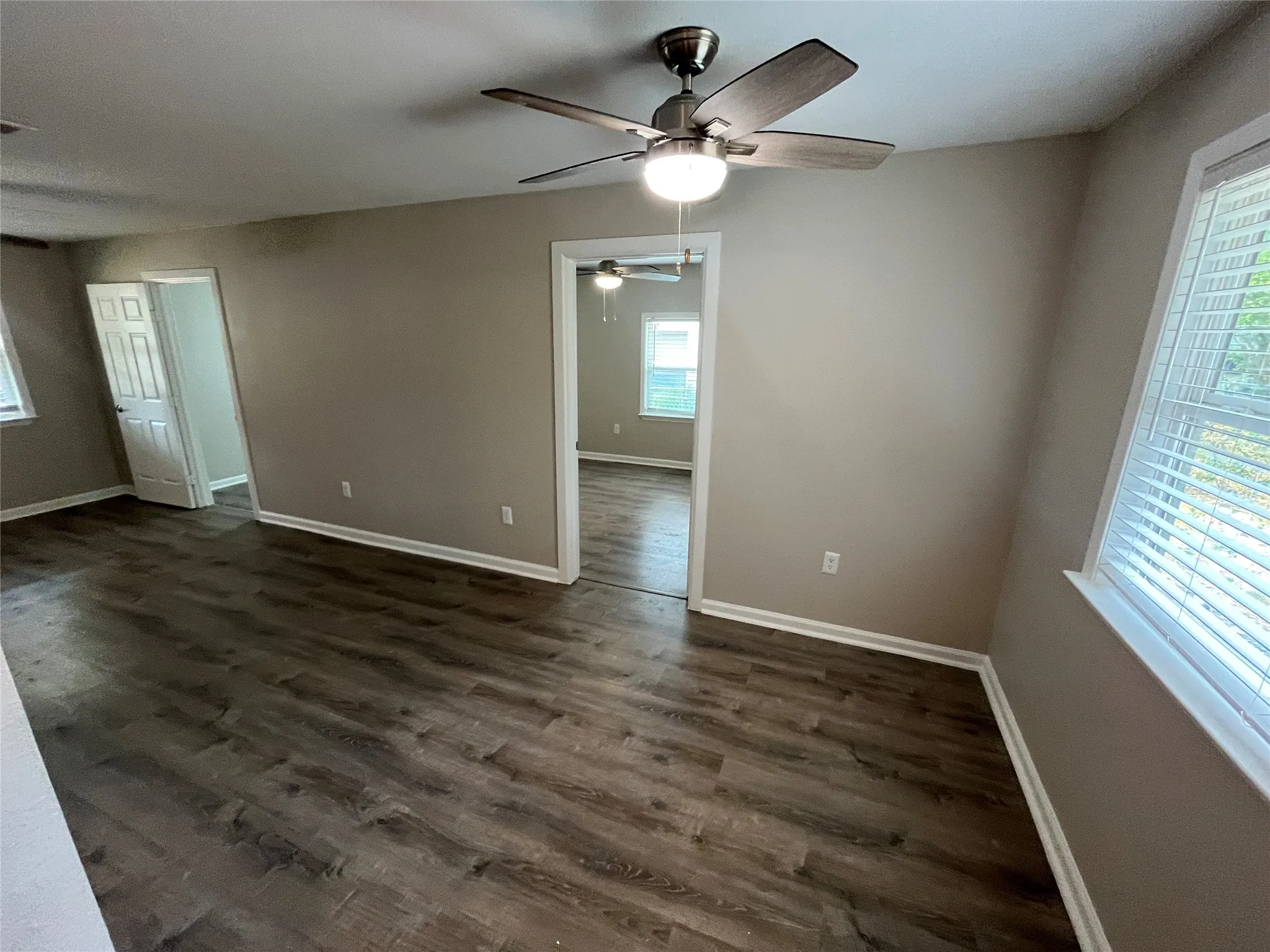 Wood-finish flooring, neutral wall paint, white trim, ceiling fan with integrated lighting, and window with blinds