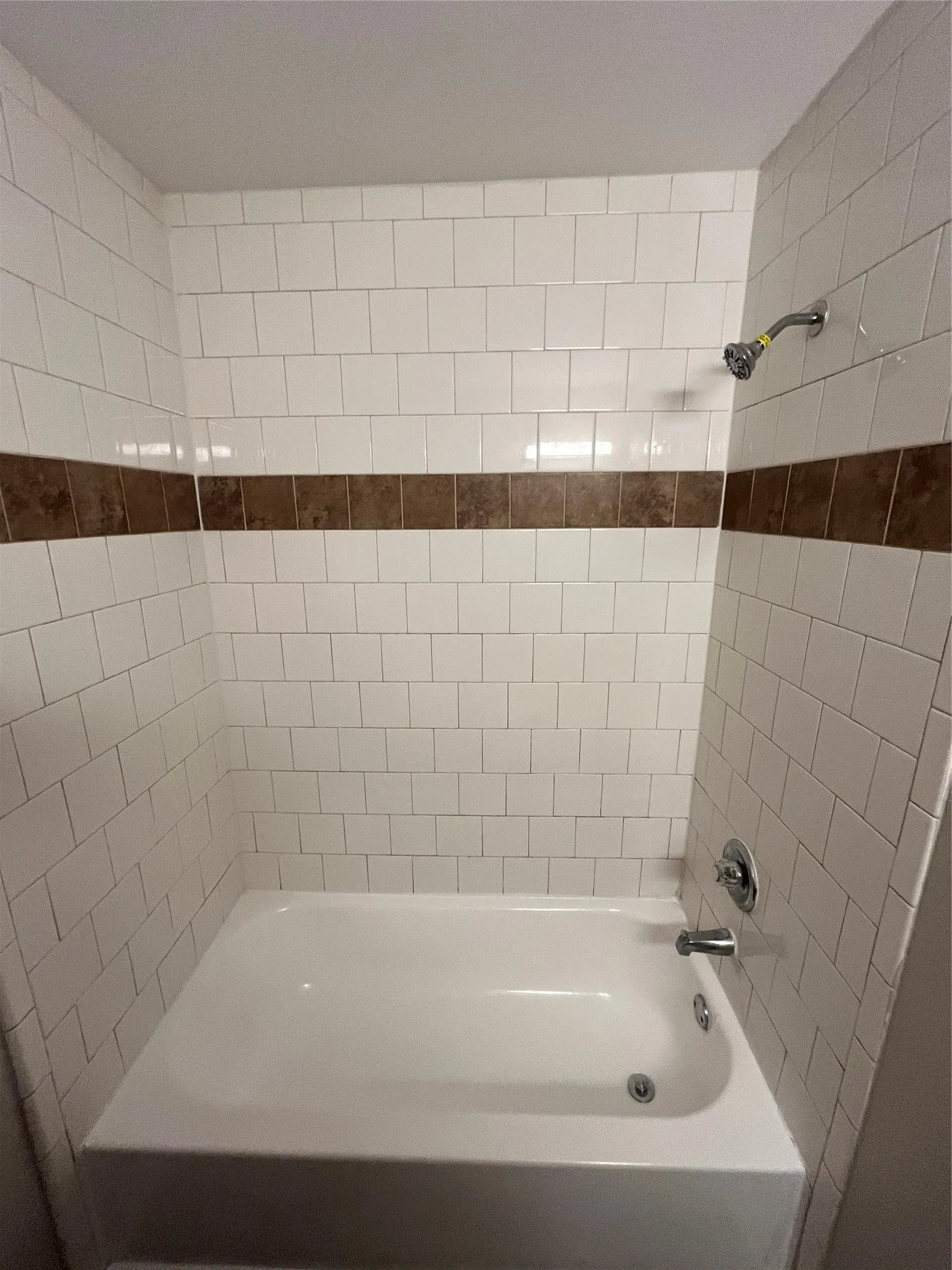 Bathtub with white subway tile surround, accented by a brown tile band, and chrome fixtures