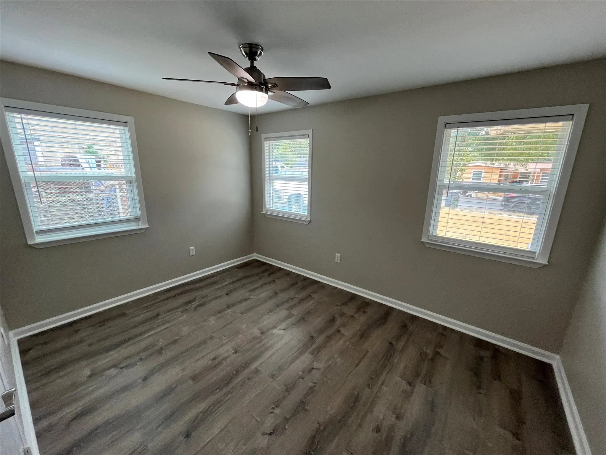 Wood-finish flooring, neutral wall tones, white trim, two windows with blinds, and a ceiling fan with integrated lighting