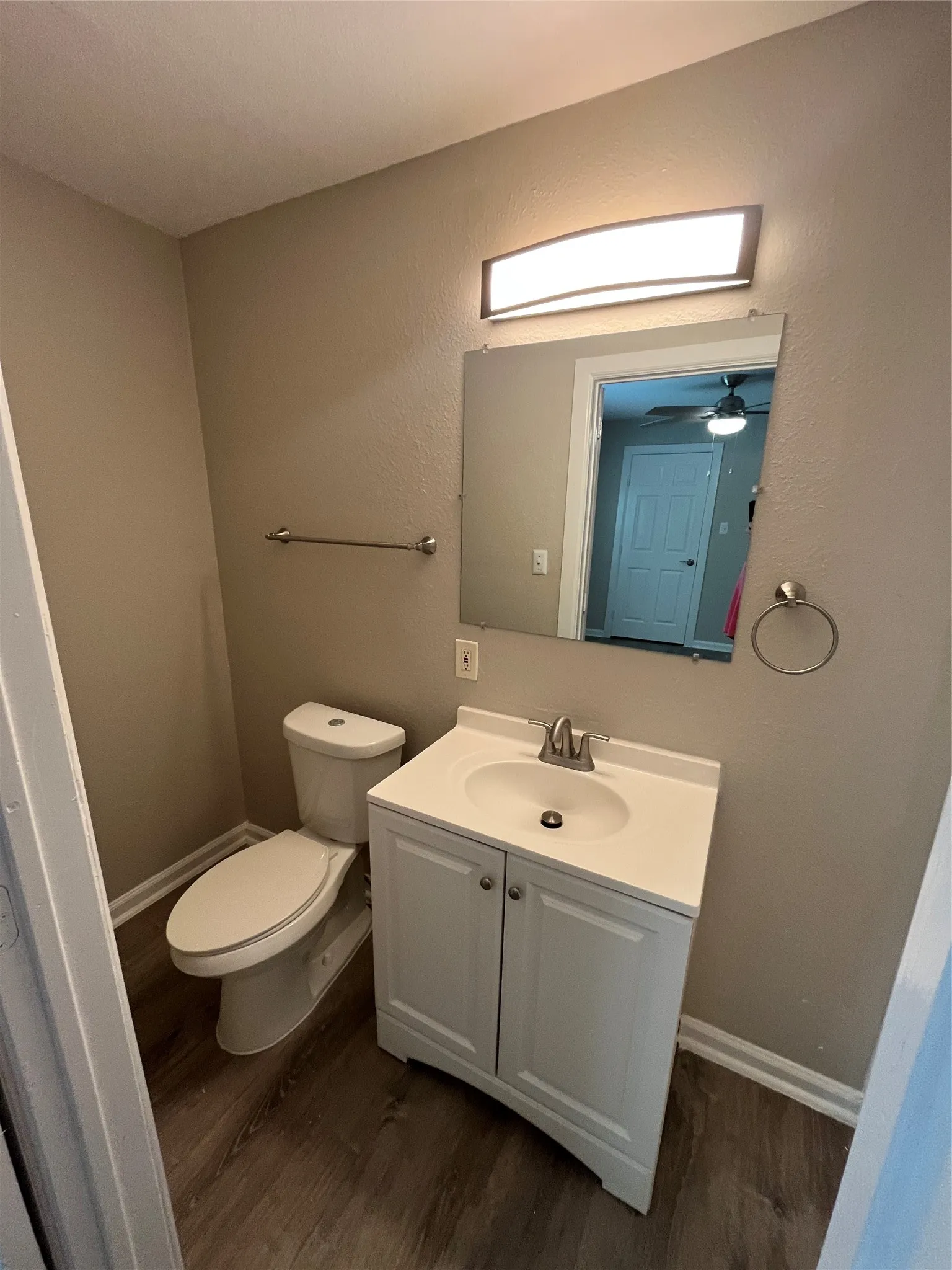 Modern vanity with integrated sink, wood-finish flooring, and wall-mounted lighting