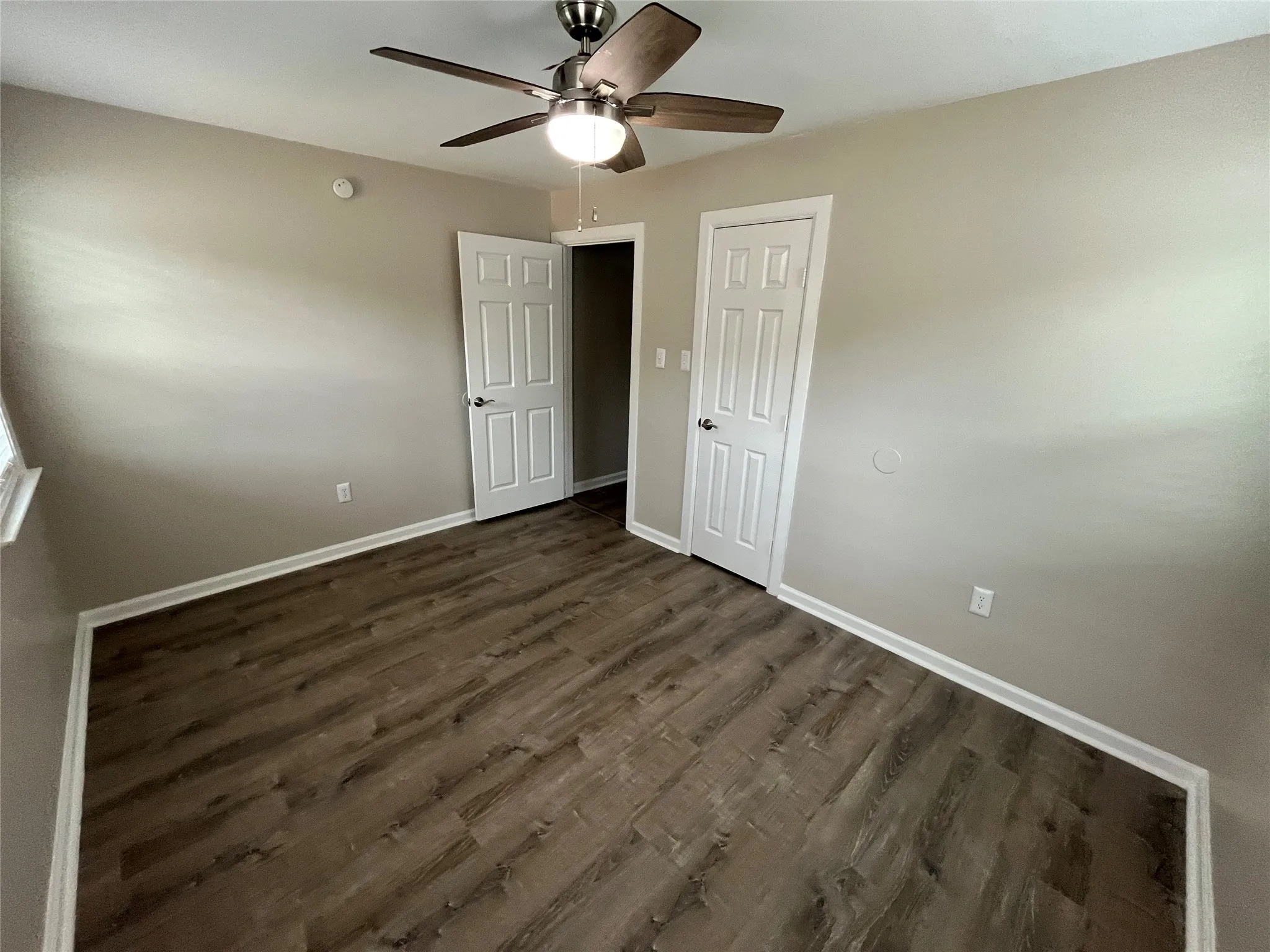 Wood-finish flooring, ceiling fan with integrated lighting, multiple paneled doors, and white trim
