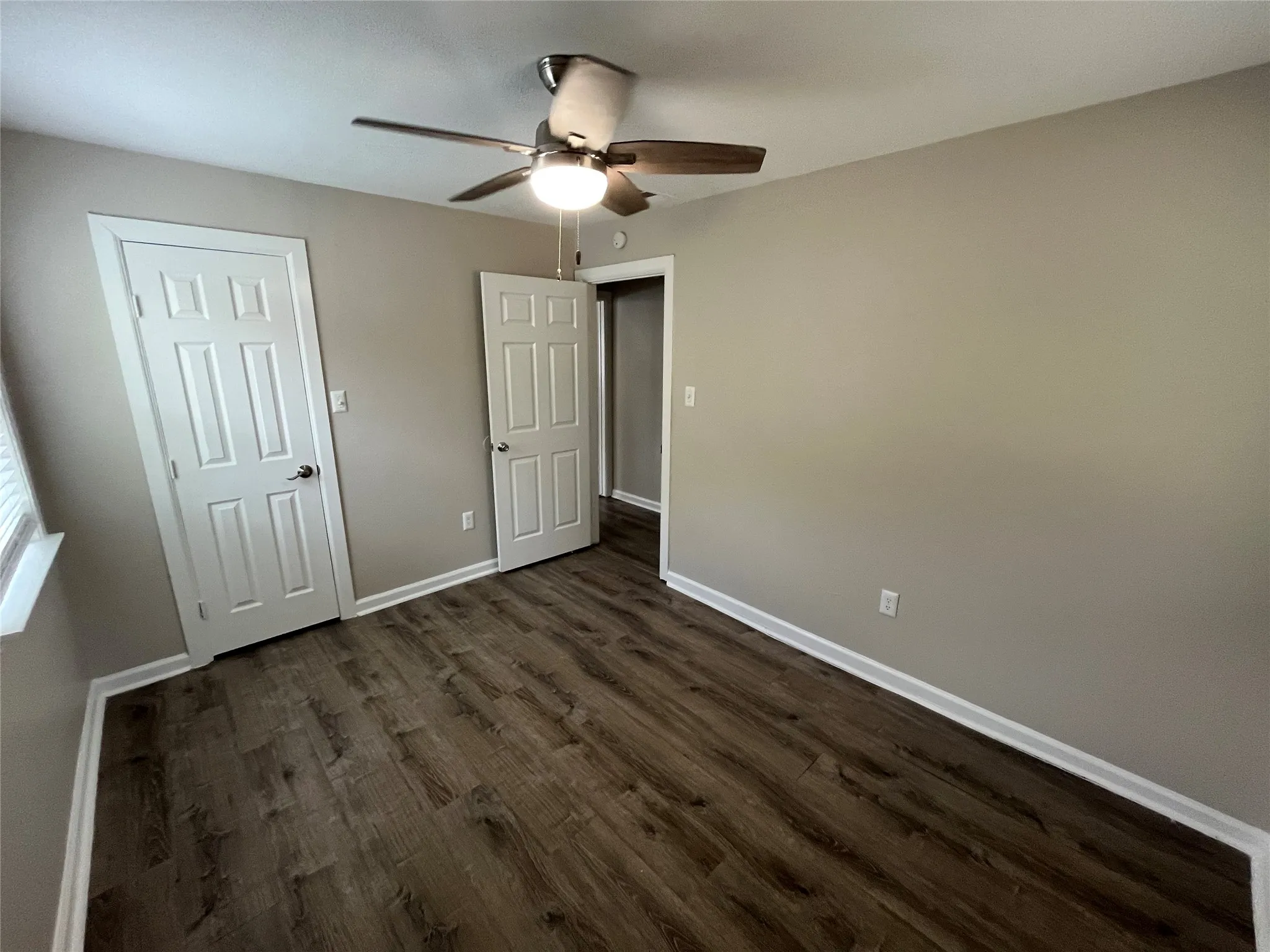 Wood-finish flooring, neutral wall tones, white trim, and a ceiling fan with integrated lighting