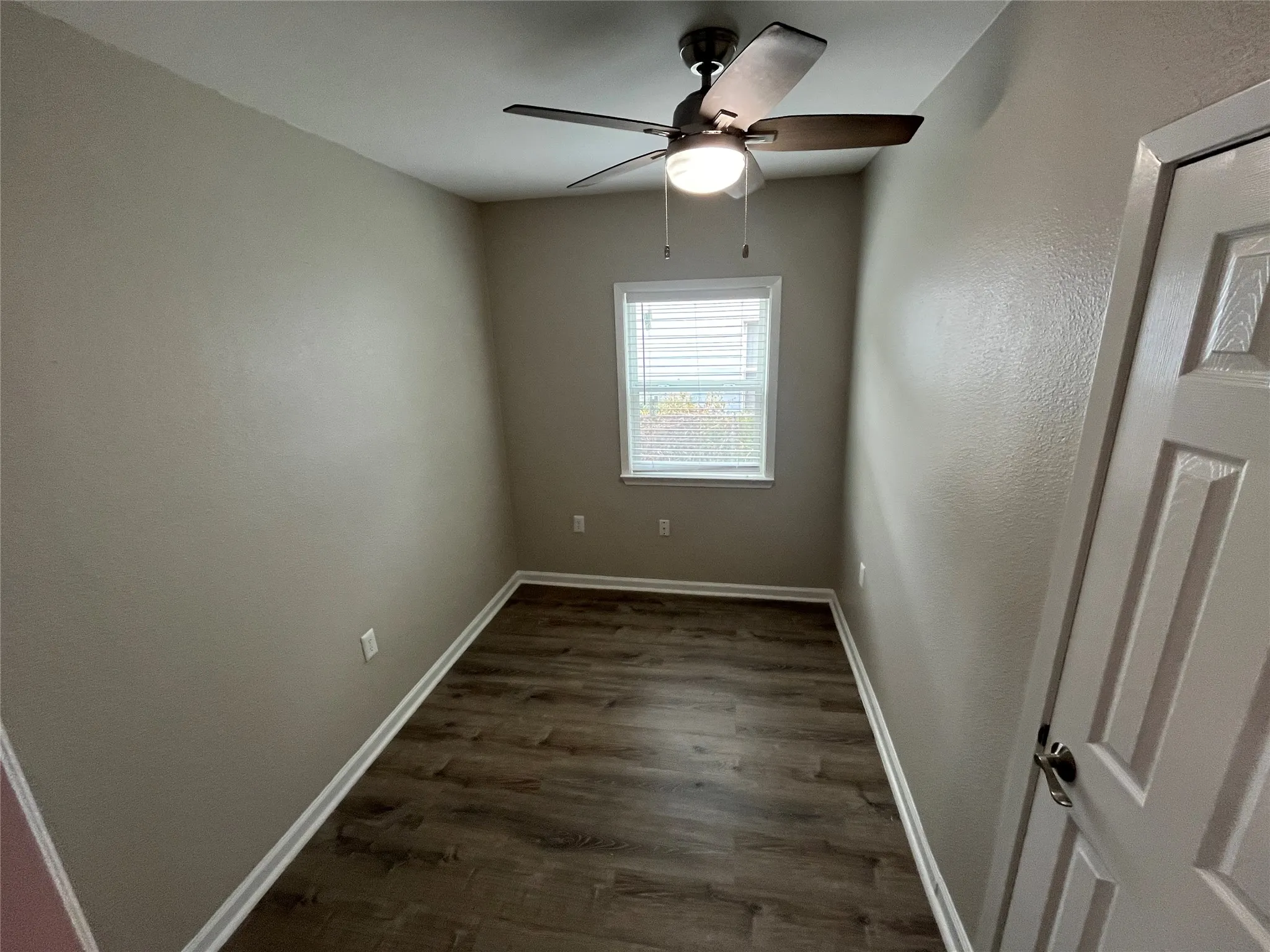 Wood-finish flooring, neutral wall tones, window with blinds, and ceiling fan with integrated lighting
