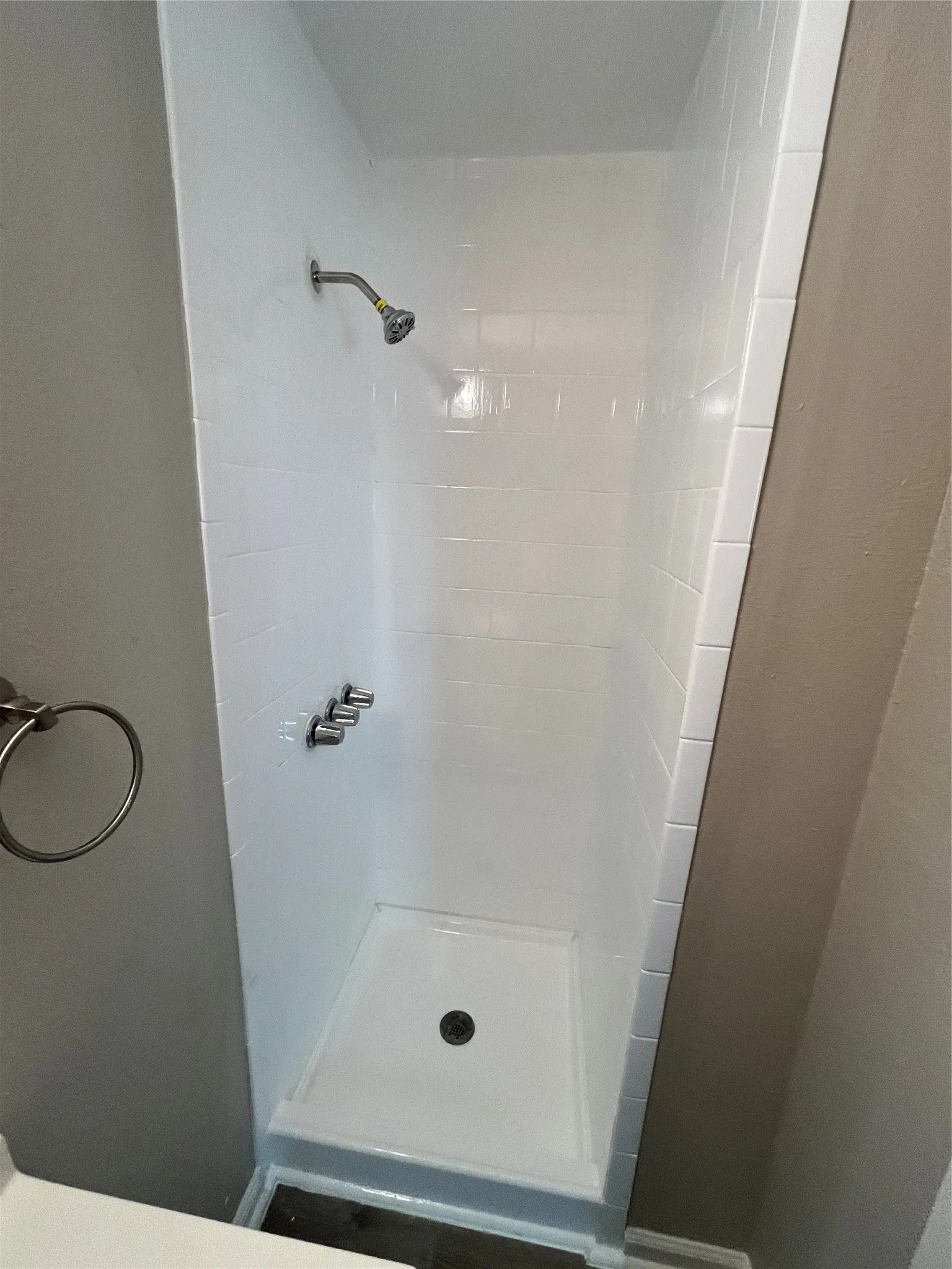 White tile shower with a single showerhead and a dark drain